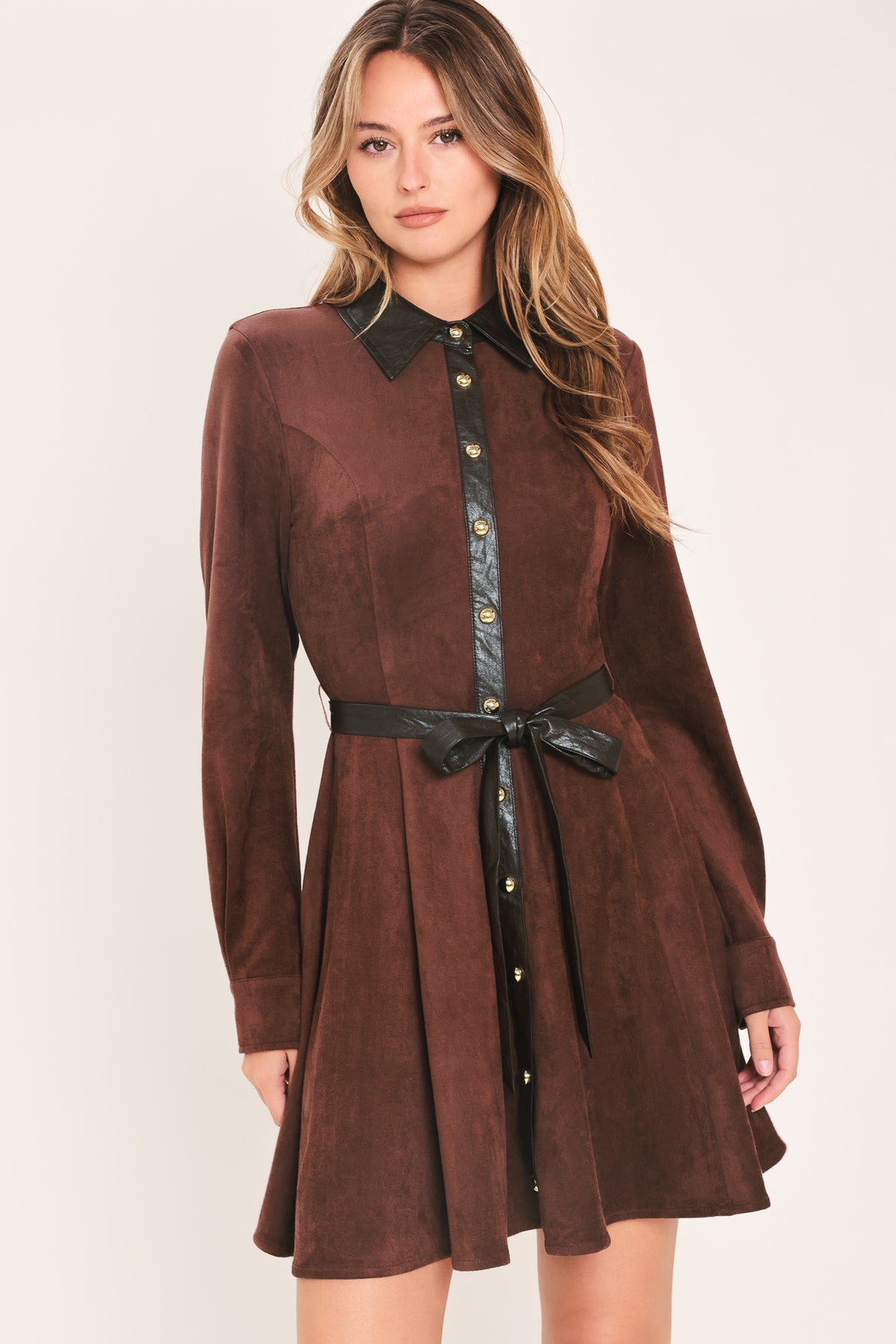 A woman modeling a brown suede long-sleeve shirt dress with a black faux-leather collar, button placket, and matching black tie belt | Flying Tomato