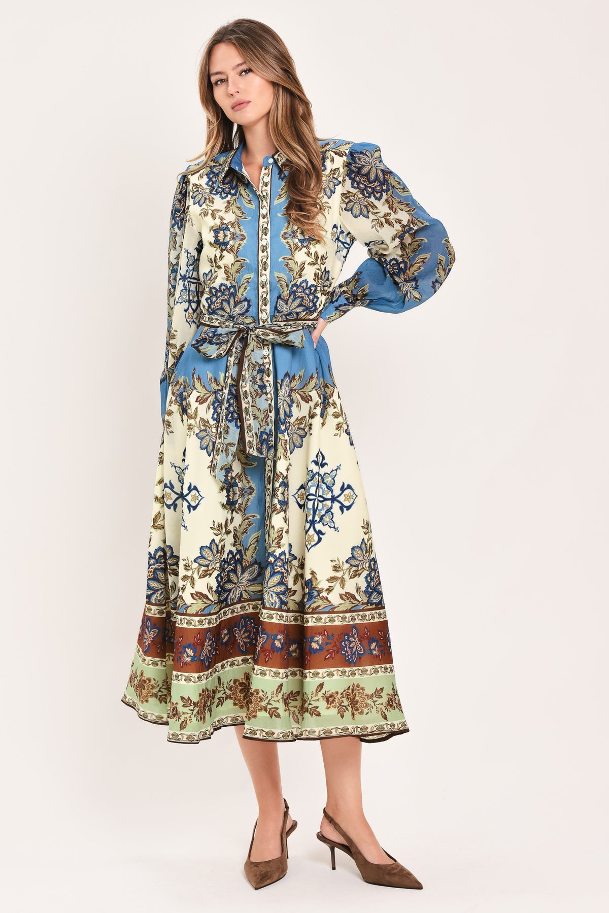 A woman wearing a long-sleeved midi dress with a blue, beige, and brown floral pattern, featuring a tie waist belt | Flying Tomato
