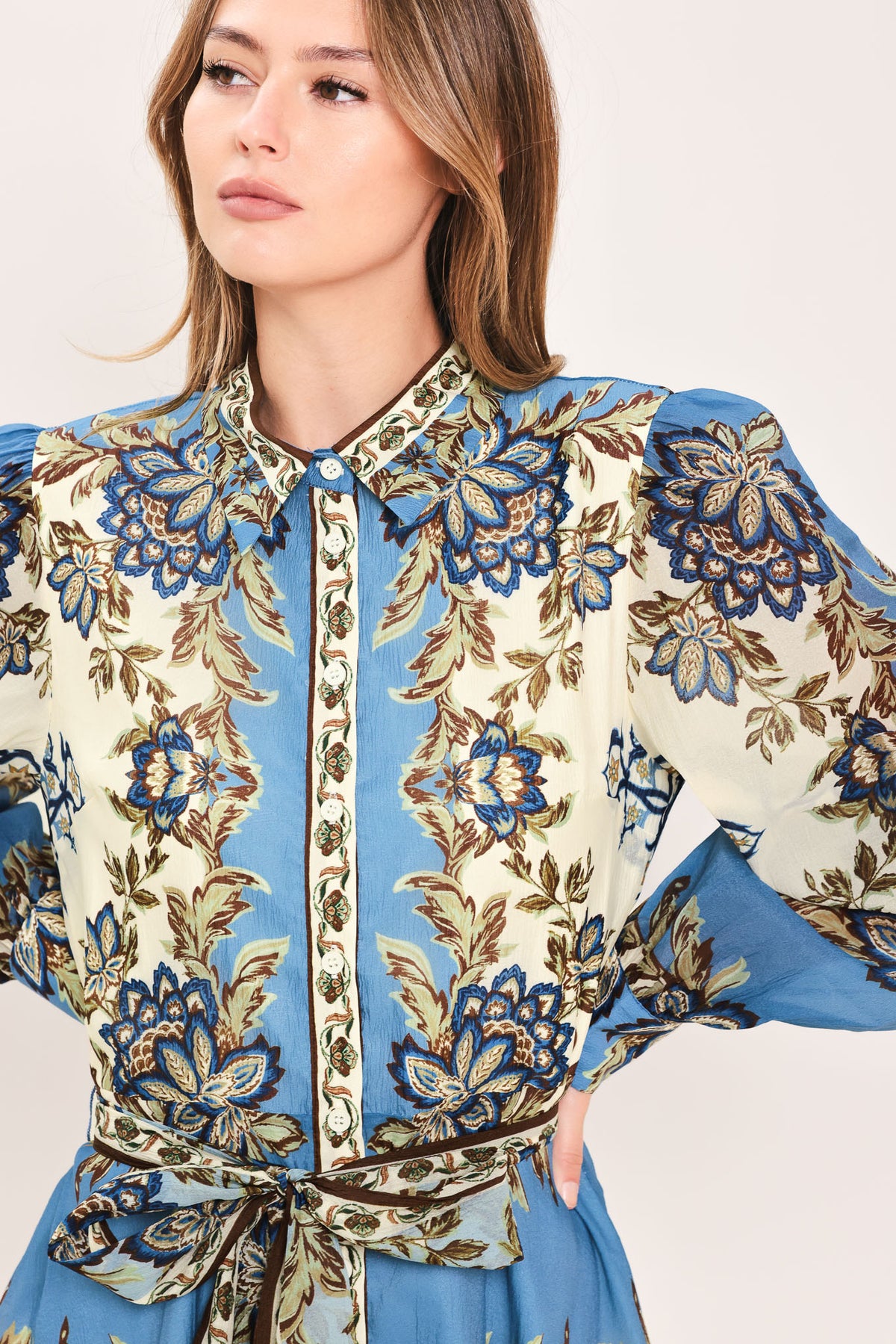 A woman wearing a long-sleeved midi dress with a blue, beige, and brown floral pattern, featuring a tie waist belt | Flying Tomato