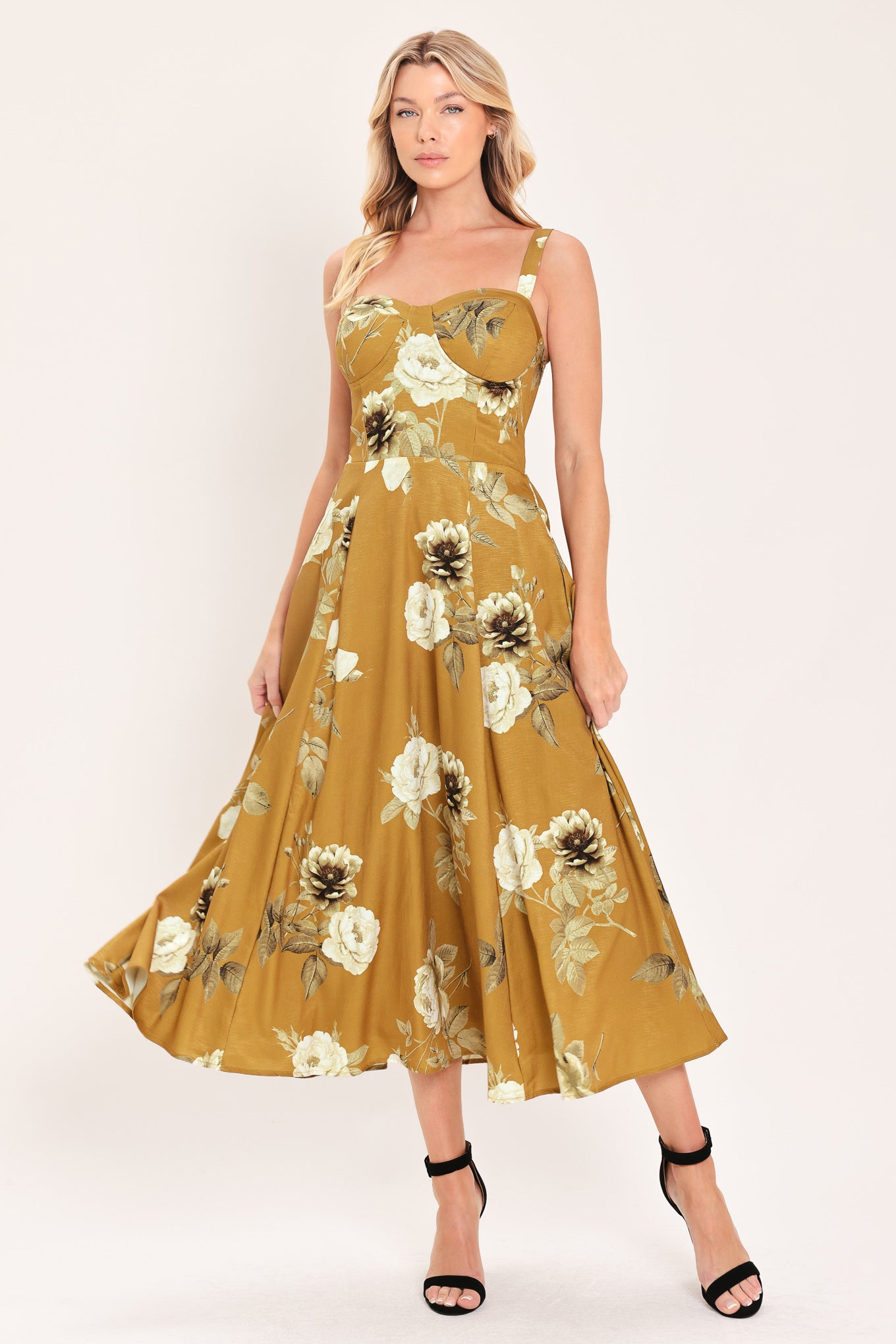A woman modeling a sleeveless midi dress with a floral print in mustard yellow, cream, and olive green | Flying Tomato