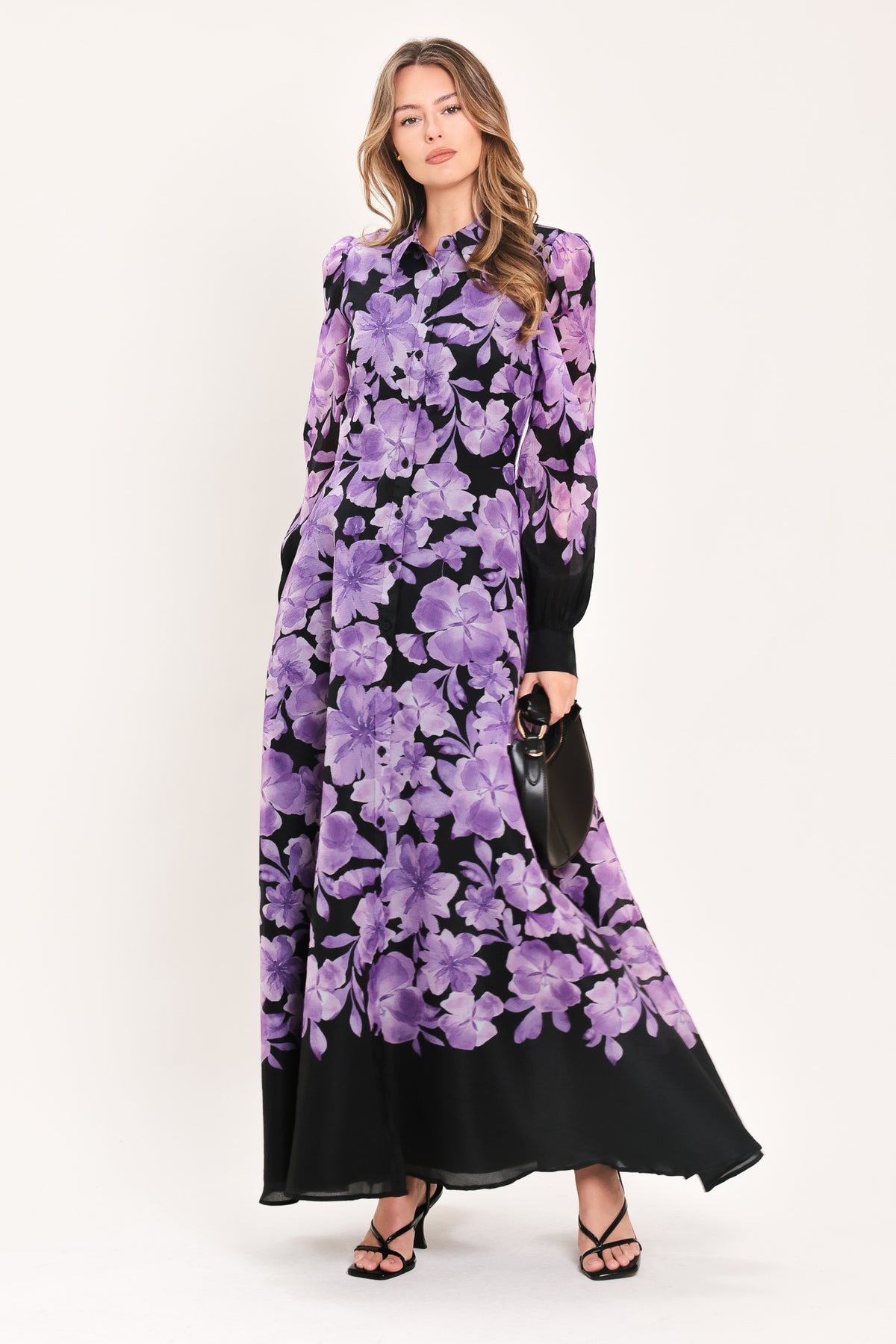A woman modeling a long-sleeved maxi dress with a black base and a large purple floral print | Flying Tomato