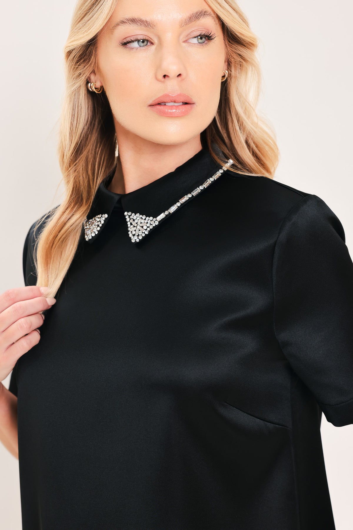 A woman modeling a black short-sleeve satin dress with a decorative silver collar | Flying Tomato