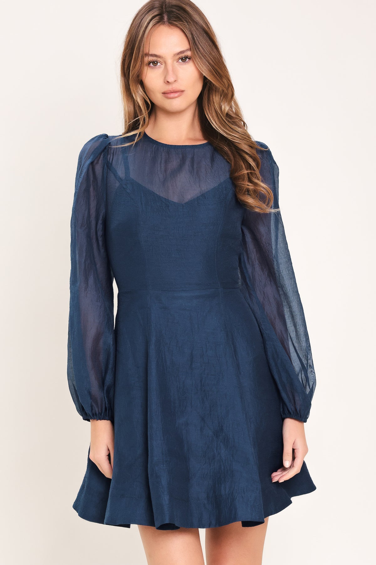 Woman wearing a blue mini dress with sheer long sleeves featuring round neckline, long sleeve, circle skirt and back zipper closure | Flying Tomato