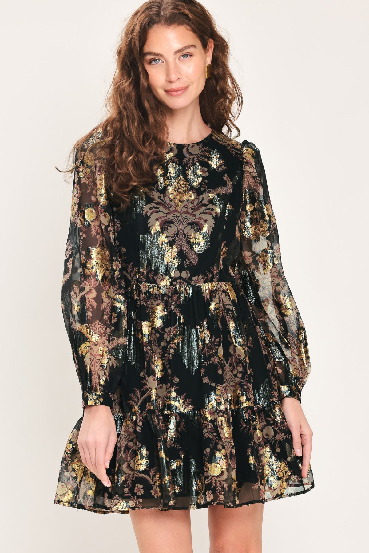 Woman wearing a black long sleeve mini dress with metallic baroque print and tiered skirt | Flying Tomato