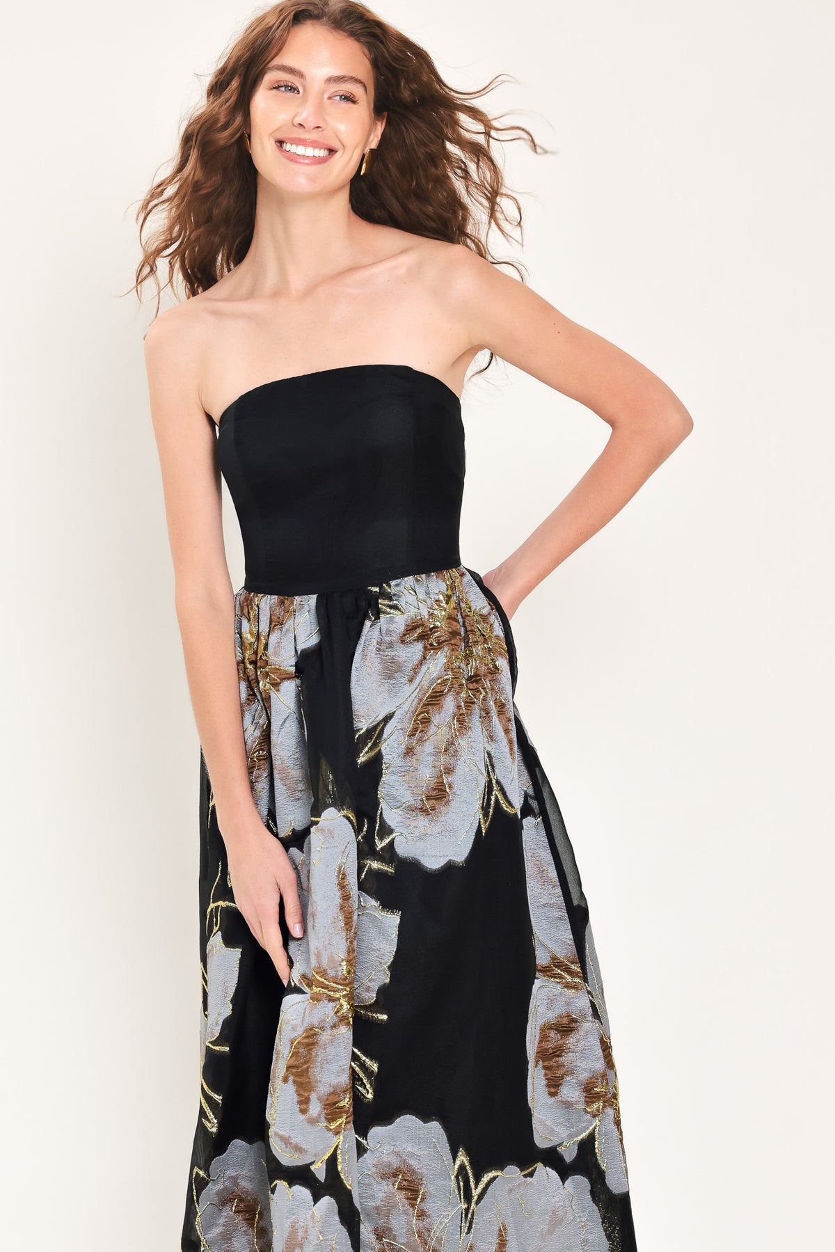 Woman wearing a strapless black maxi dress with a bluish grey floral print and gold details printed on the skirt | Flying Tomato