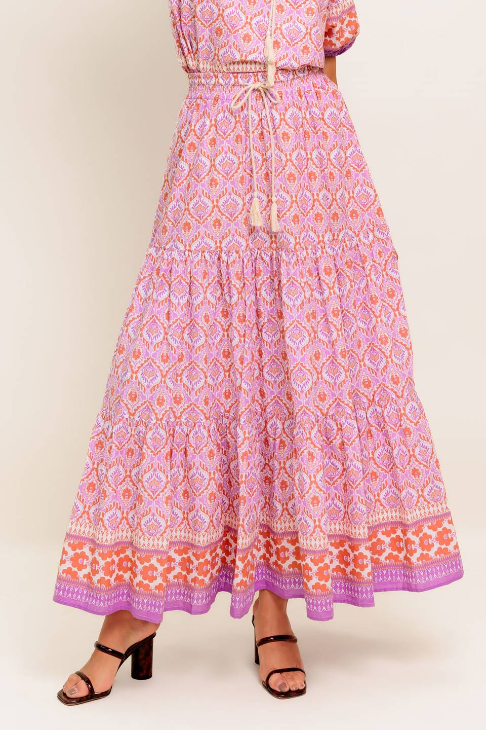 A printed woven maxi skirt featuring elasticized waist with contrasting tie and tiered bottom.
