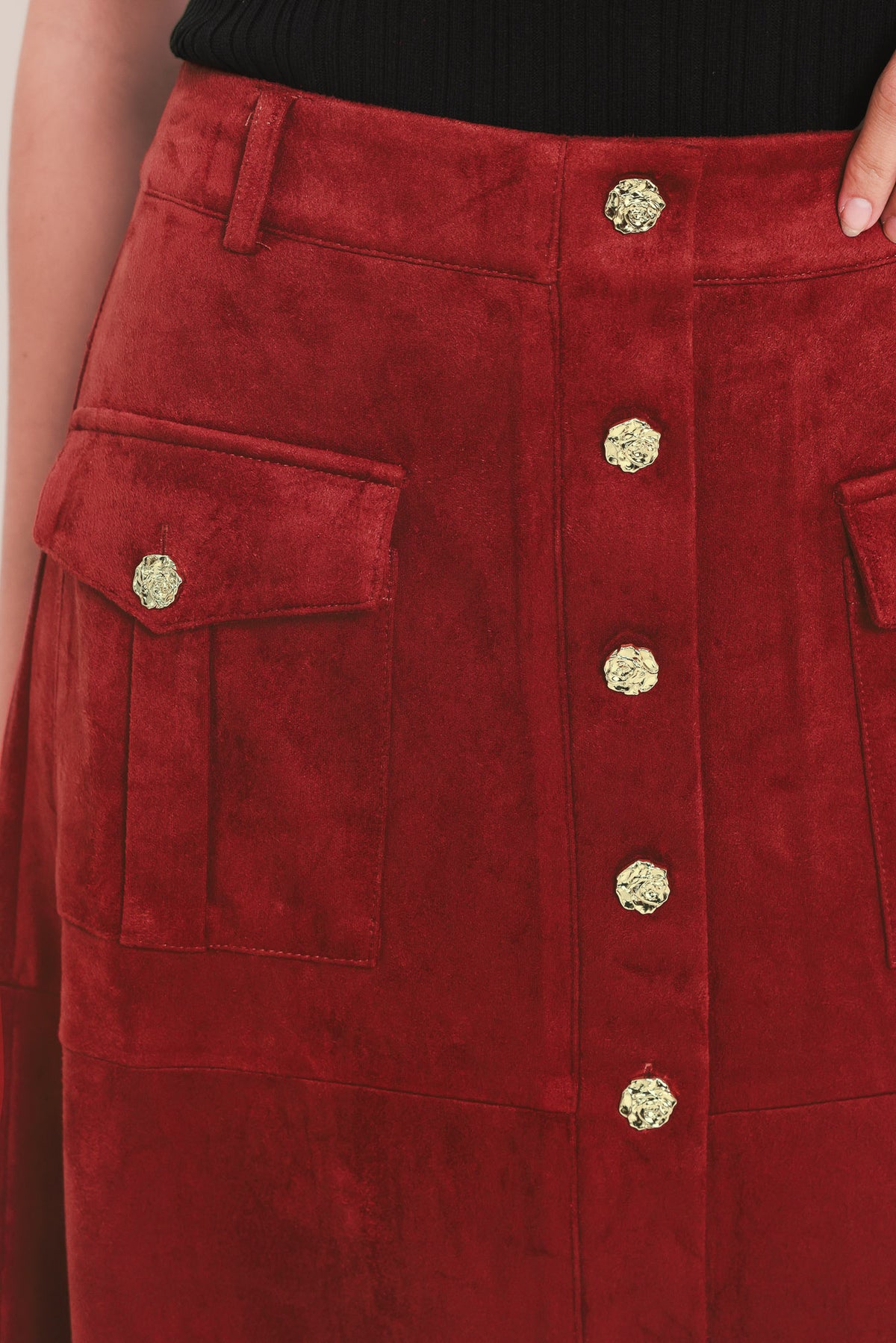 A brick colored suede midi skirt with a button-down front, flap pockets, and gold-tone button accents, shown on a model | Flying Tomato