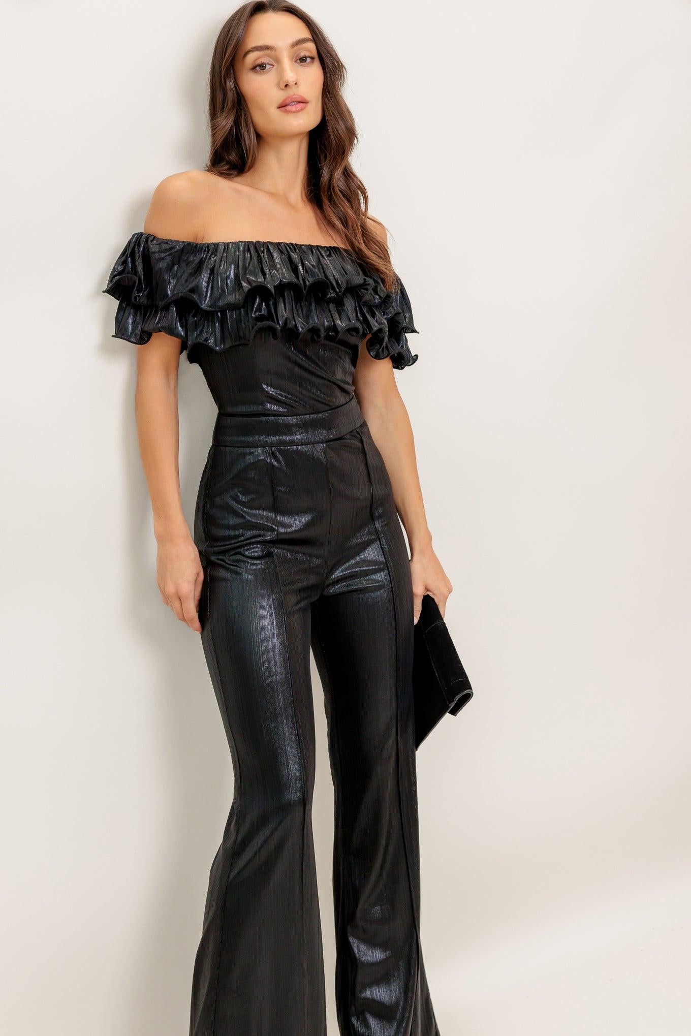 Woman wearing a black off-shoulder top and high-waisted pants against a white background