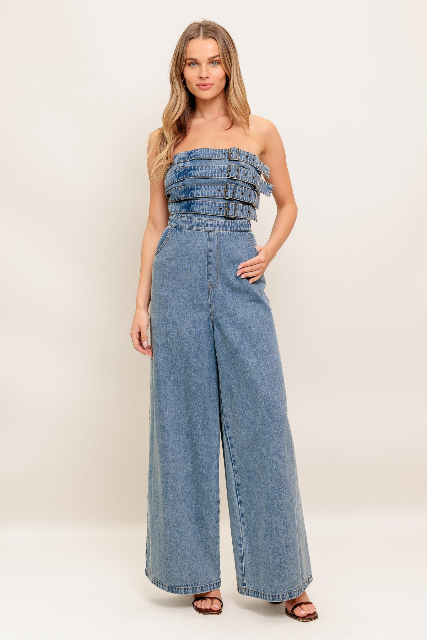 A washed denim jumpsuit featuring strapless, front buckle detail, side pockets and back zipper closure