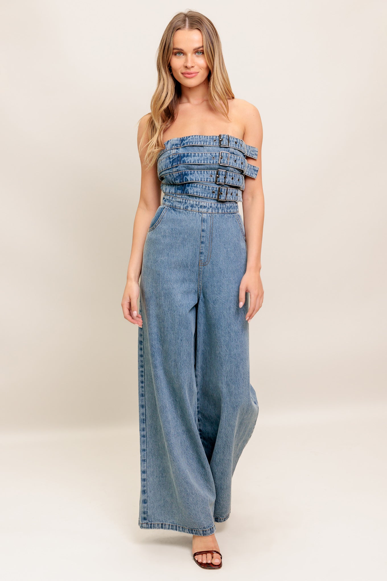 A washed denim jumpsuit featuring strapless, front buckle detail, side pockets and back zipper closure
