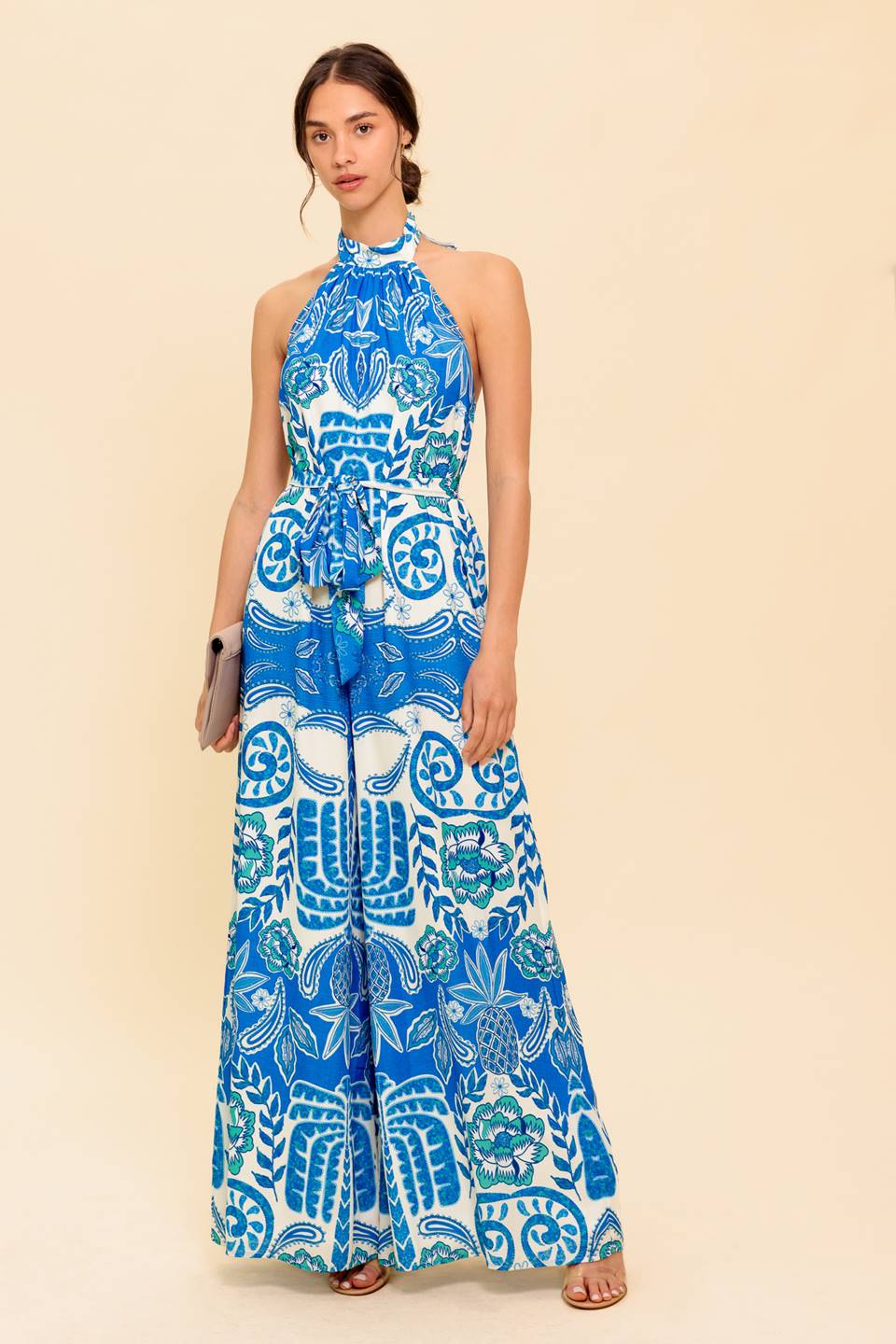 A printed woven jumpsuit featuring halter neckline with back tie, self sash tie, wide leg and bare back