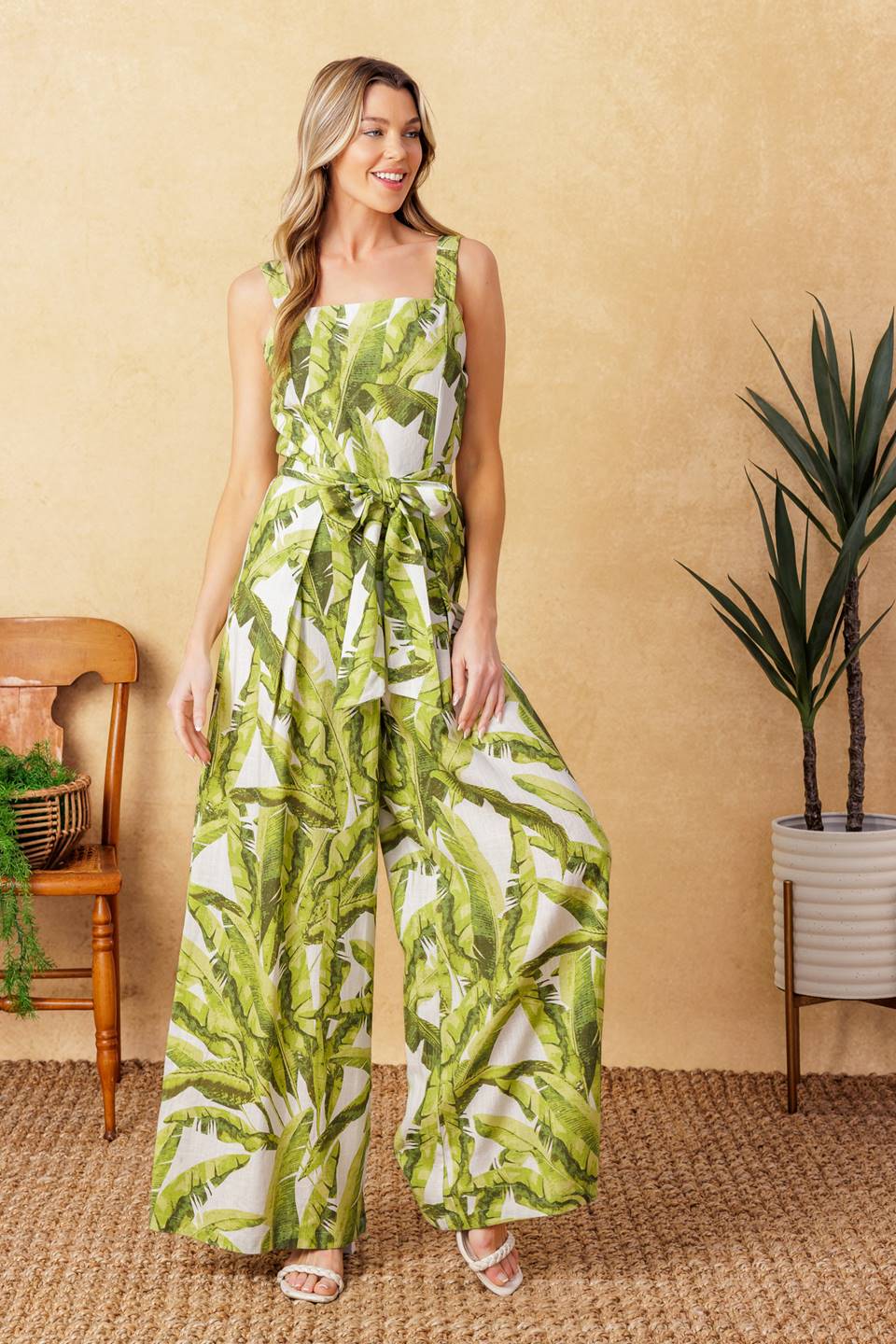 A printed woven jumpsuit featuring straight neckline, straps, self sash tie, wide leg with front pleat and back zipper closure