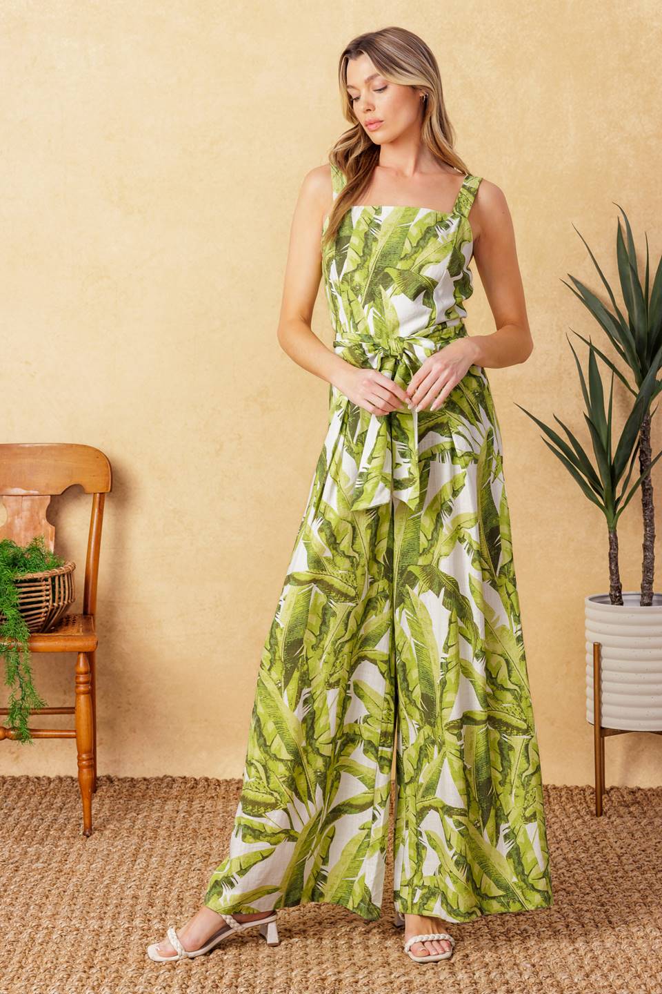 A printed woven jumpsuit featuring straight neckline, straps, self sash tie, wide leg with front pleat and back zipper closure