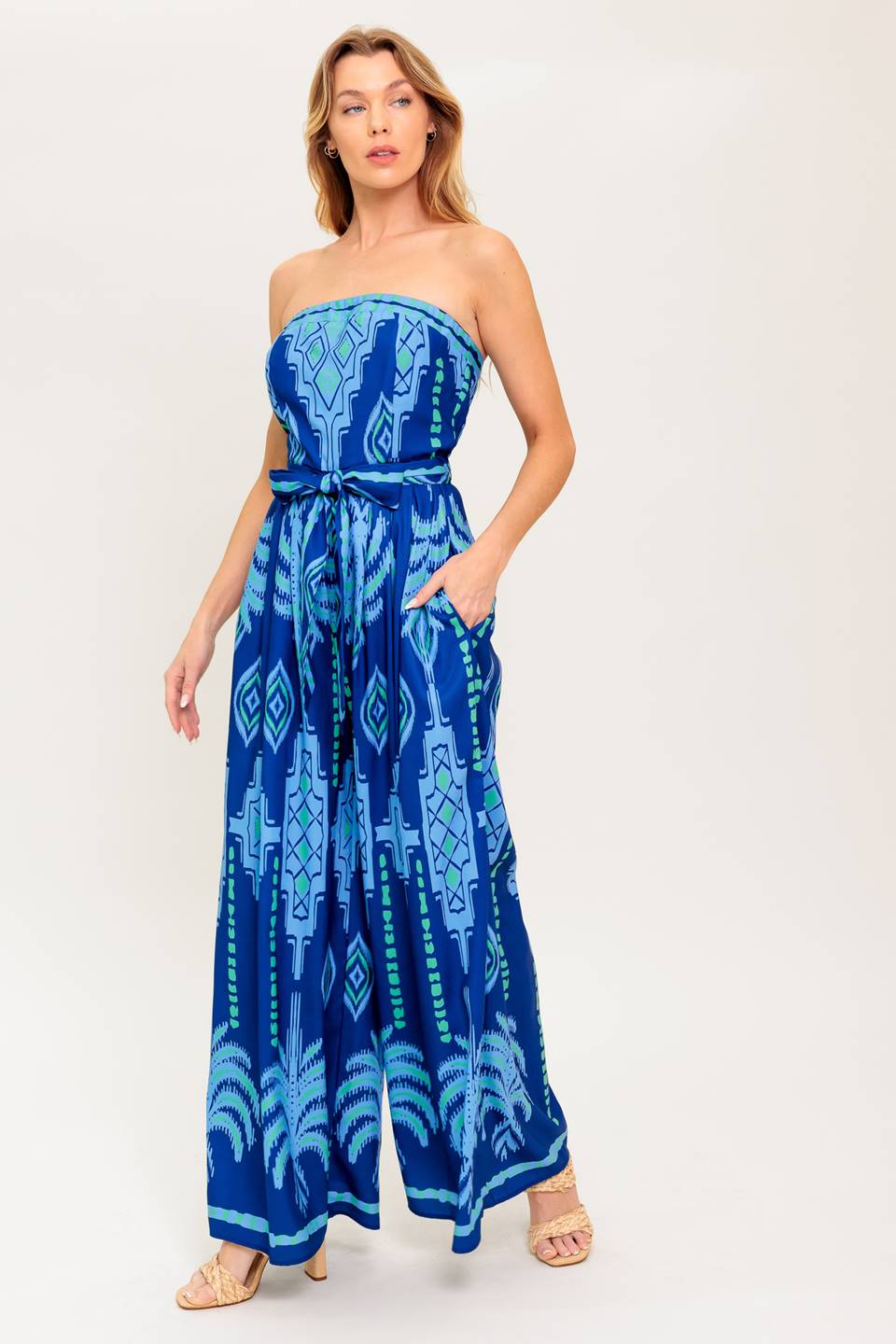 A printed woven jumpsuit featuring strapless, self sash tie, wide leg and back zipper closure