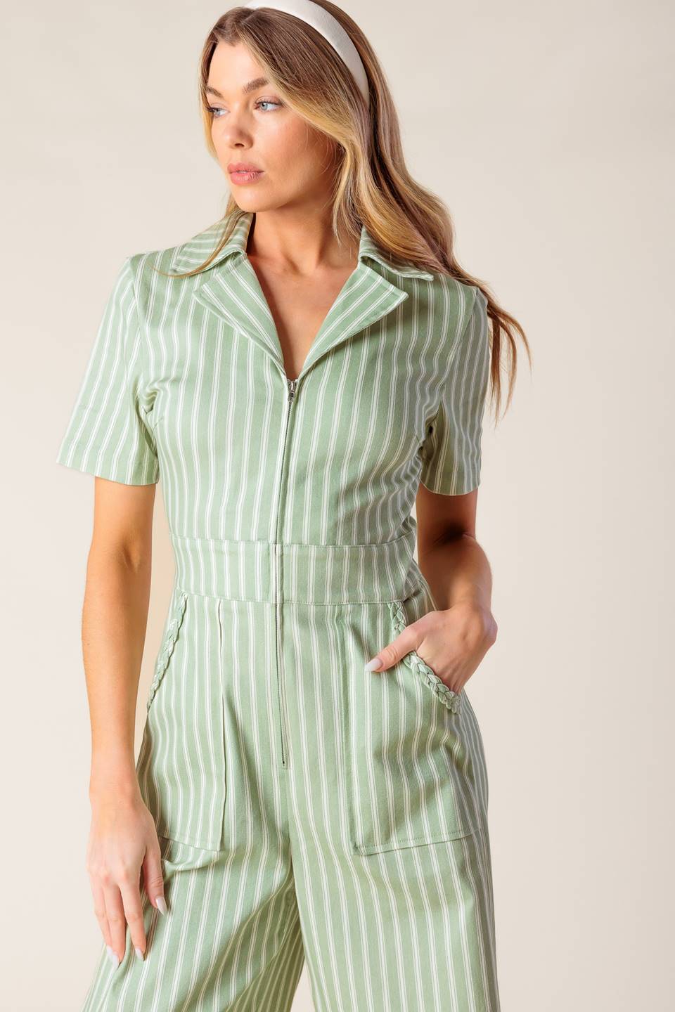 A striped woven jumpsuit featuring collar, short sleeve, zipper down front, side pocket with braided trim and wide leg