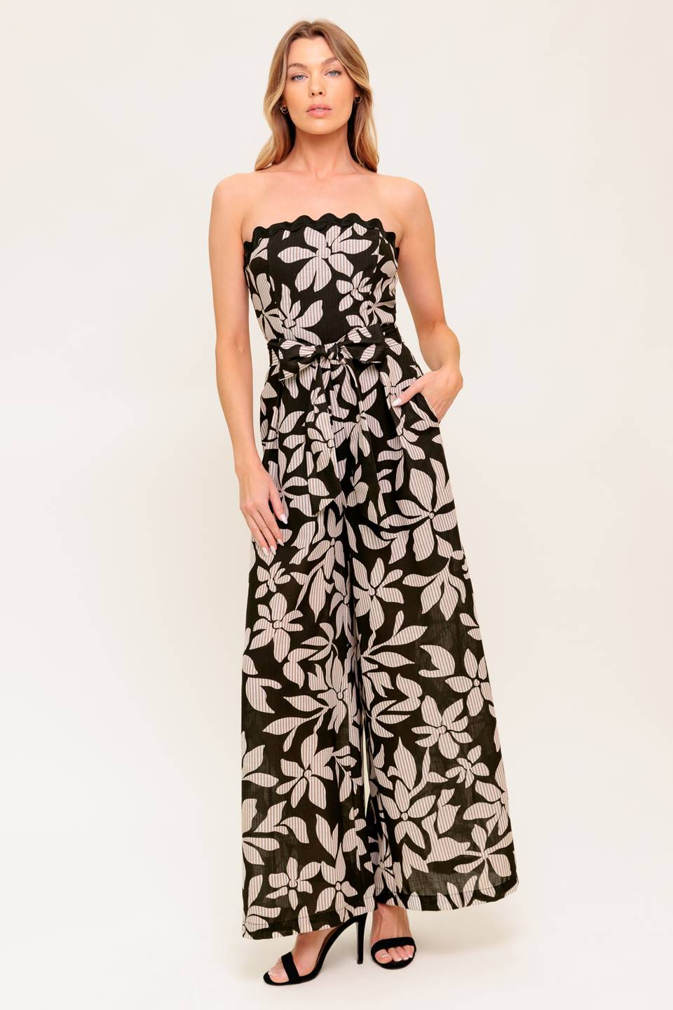 A printed woven jumpsuit featuring strapless neckline with ric rac trimmed edge, self sash tie, wide leg and back zipper closure.
