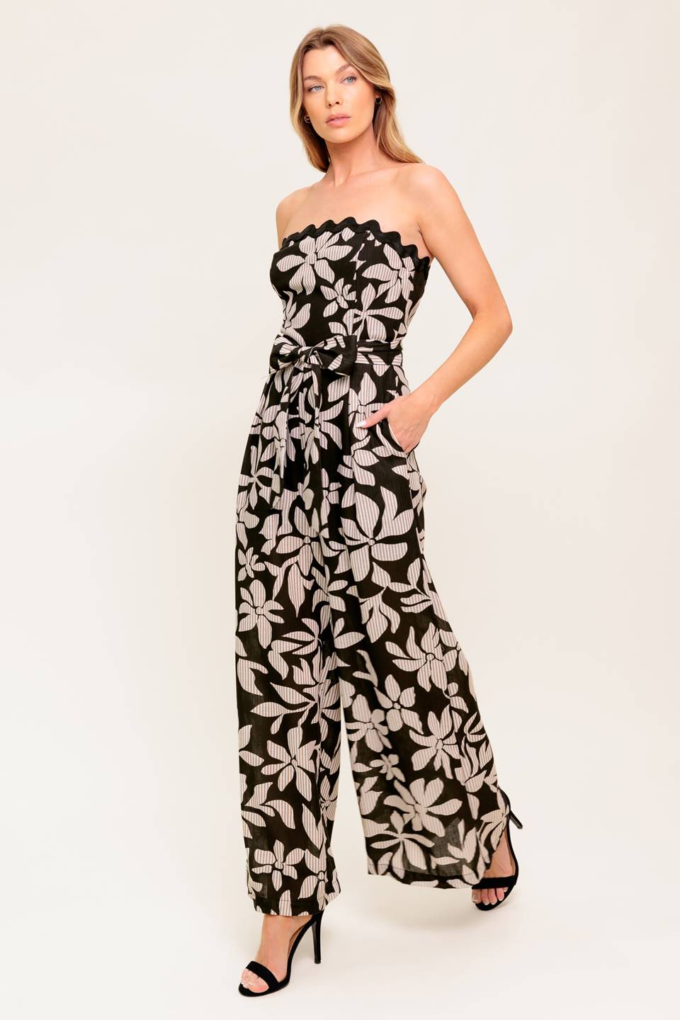 A printed woven jumpsuit featuring strapless neckline with ric rac trimmed edge, self sash tie, wide leg and back zipper closure.