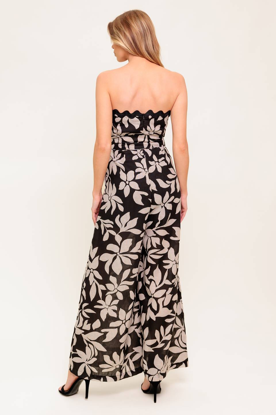 A printed woven jumpsuit featuring strapless neckline with ric rac trimmed edge, self sash tie, wide leg and back zipper closure.