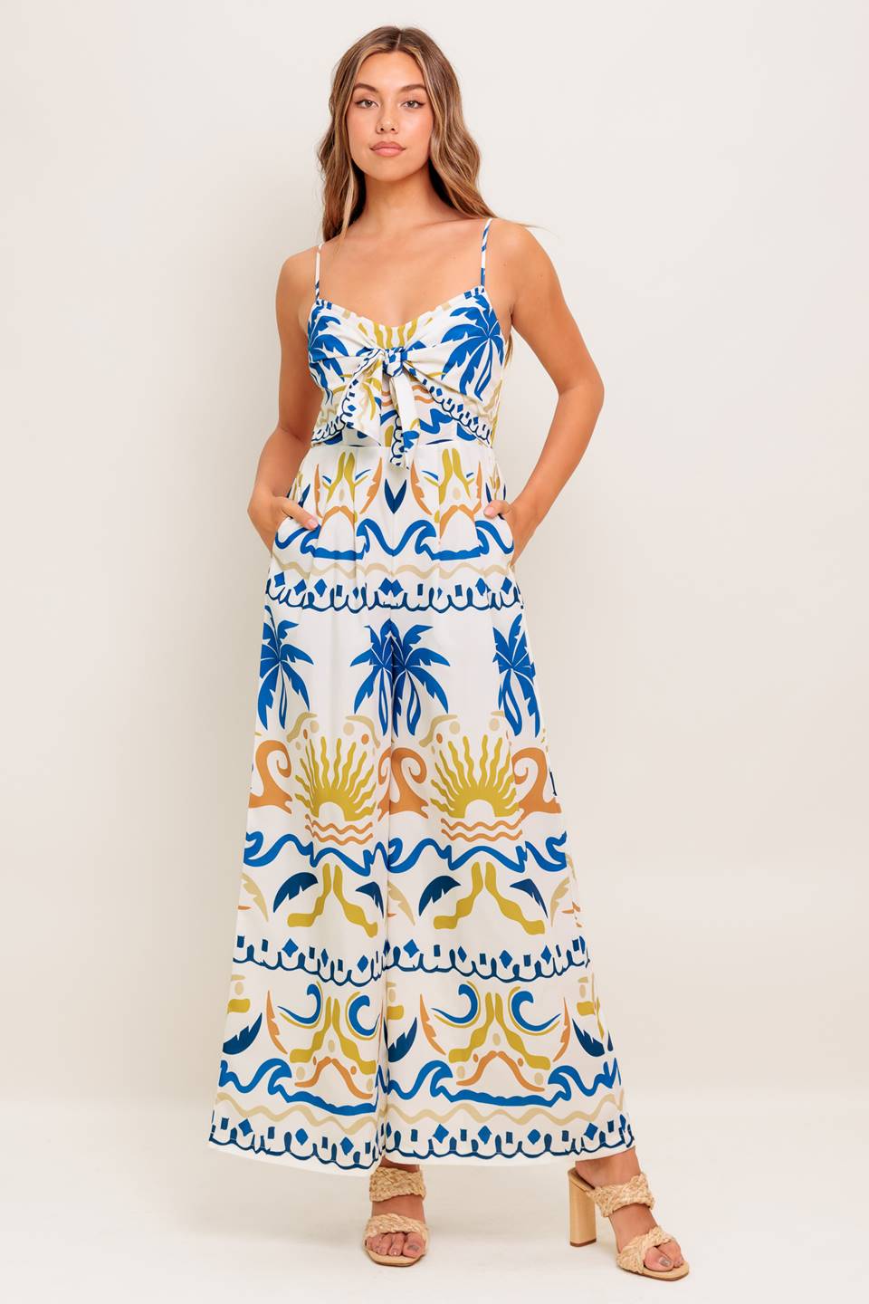 A printed woven jumpsuit featuring cami top with front tie detail, straps, wide leg and smocked back bodice