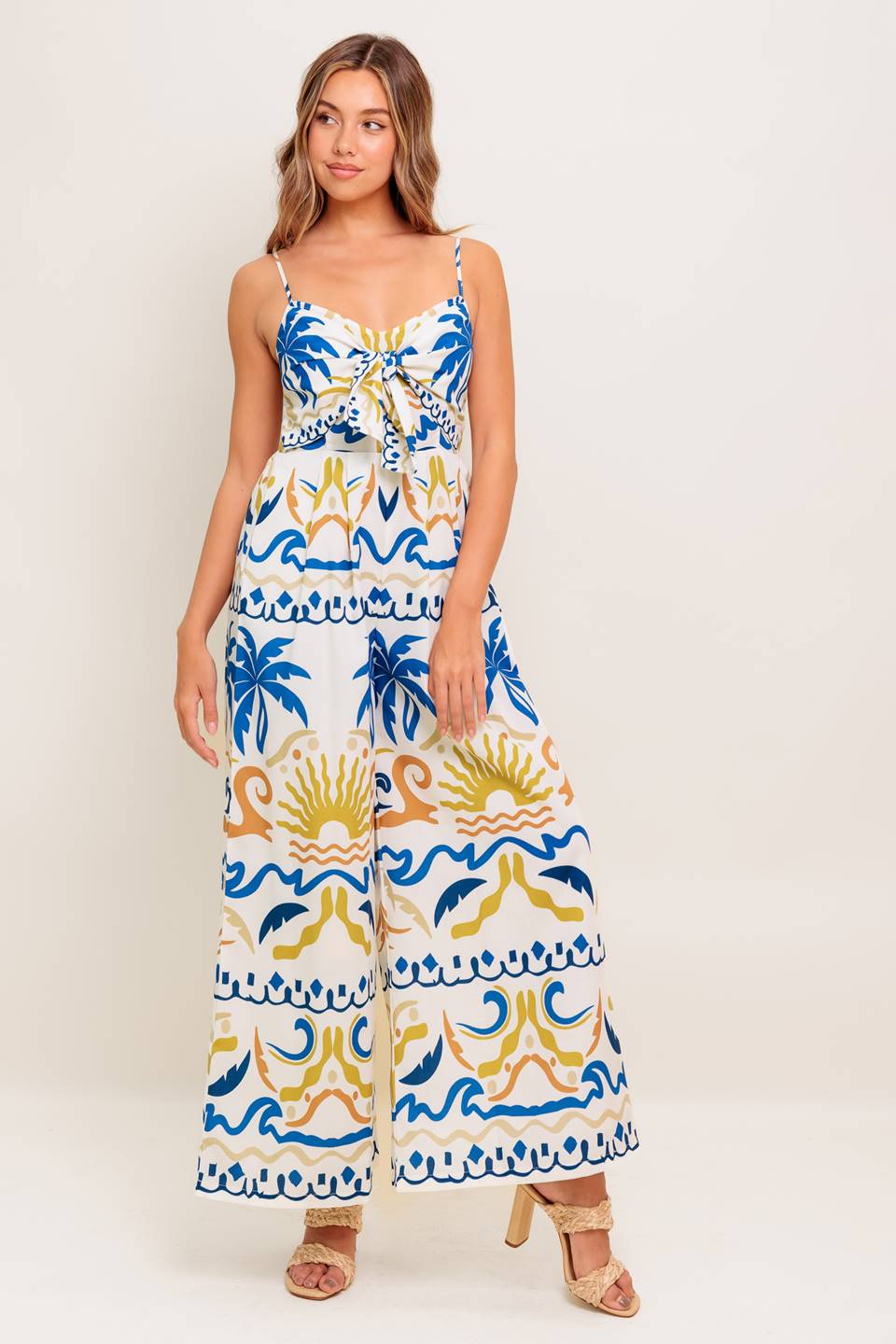 A printed woven jumpsuit featuring cami top with front tie detail, straps, wide leg and smocked back bodice