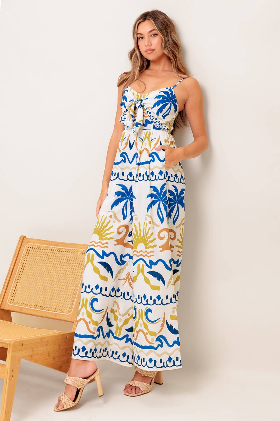 A printed woven jumpsuit featuring cami top with front tie detail, straps, wide leg and smocked back bodice