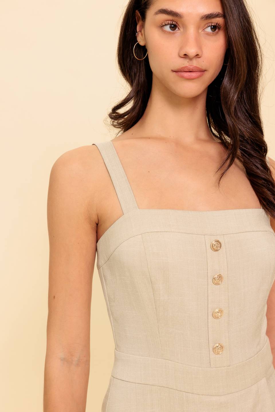 A solid woven romper featuring straight neckline, straps, front button detail, skort bottom and back zipper closure