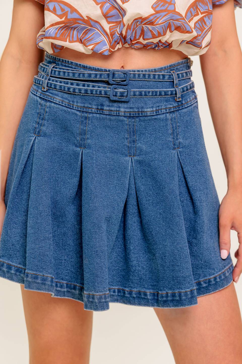 A washed denim skort featuring double self belt, inverted pleats and side zipper closure