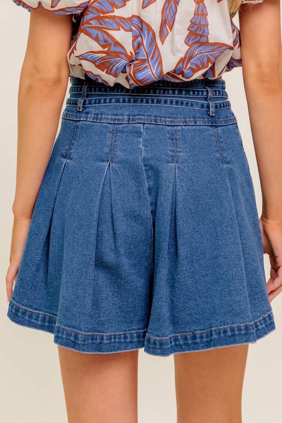 A washed denim skort featuring double self belt, inverted pleats and side zipper closure