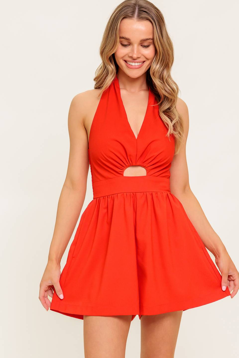 A solid red woven romper featuring halter neckline, front cut out and smocked back bodice