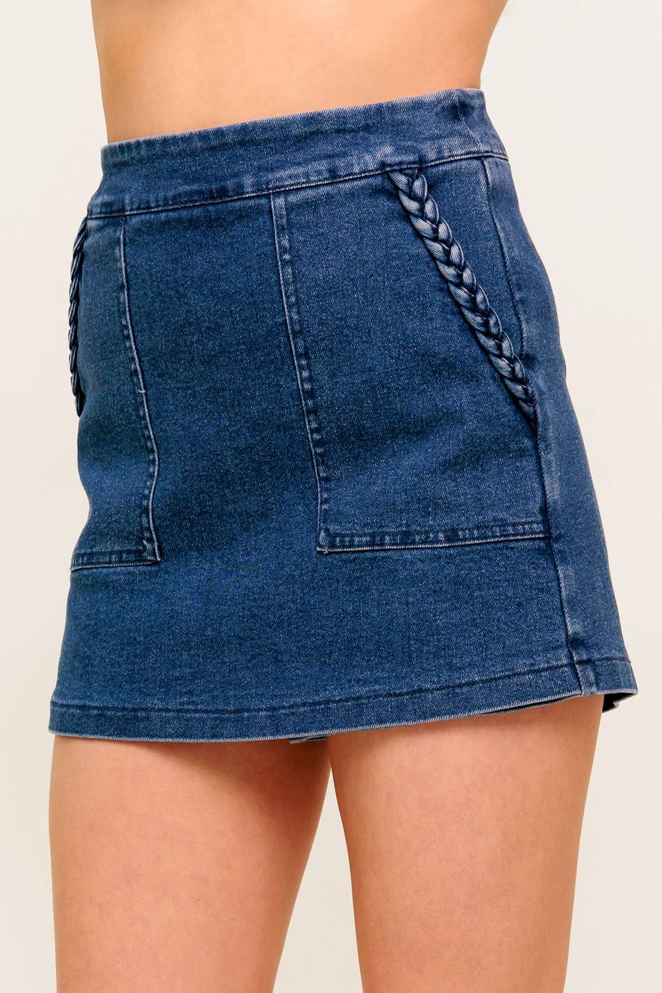A washed denim skort featuring side pocket with braid trim and back zipper closure.