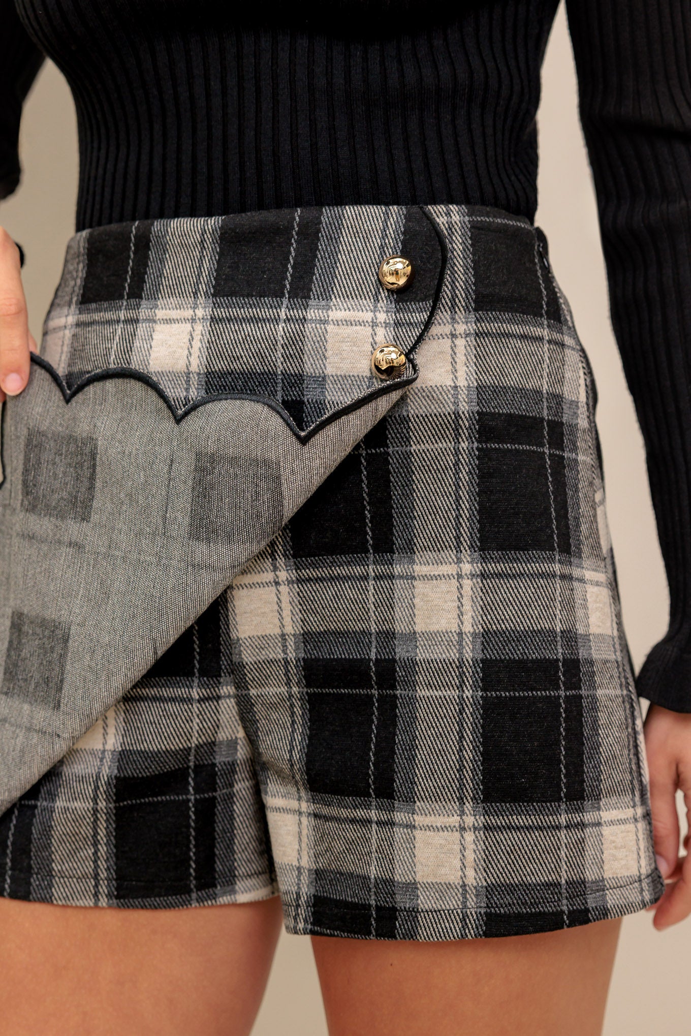 A woven plaid skort featuring front side button, scalloped edge and side zipper closure