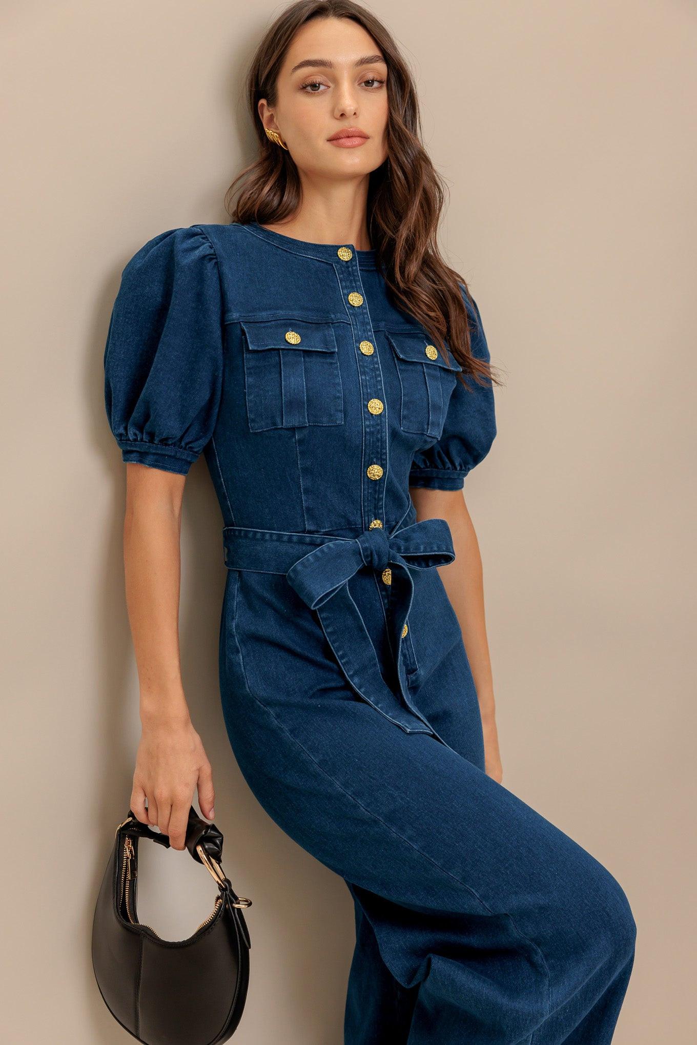 A washed denim jumpsuit featuring round neckline, short puff sleeve, front pockets, button down, self belt and wide leg