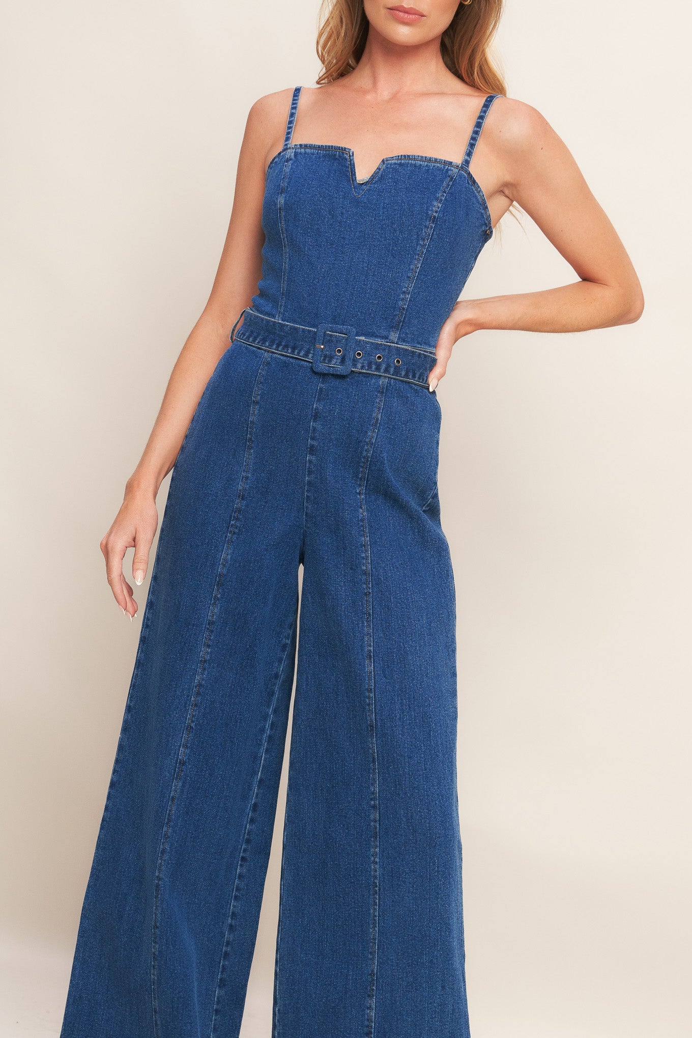 A washed denim jumpsuit featuring straight neckline with V cut out, straps, self belt, wide leg and back zipper closure