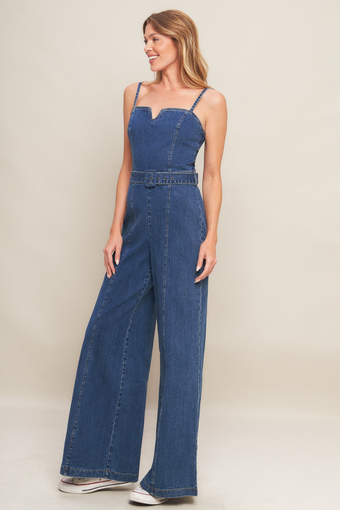 A washed denim jumpsuit featuring straight neckline with V cut out, straps, self belt, wide leg and back zipper closure