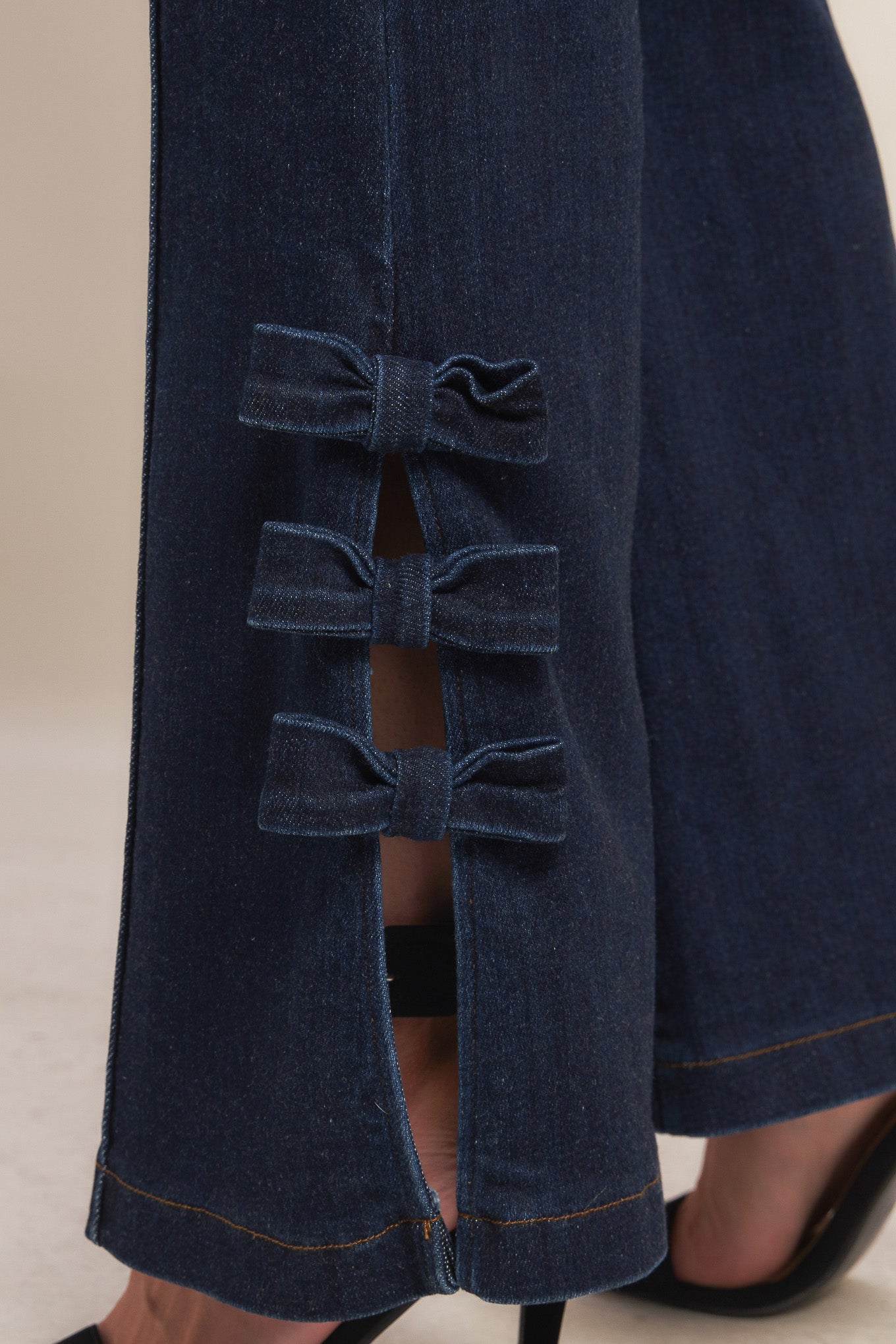 A washed denim pant featuring front closure, side pocket, flare leg with bow tie detail