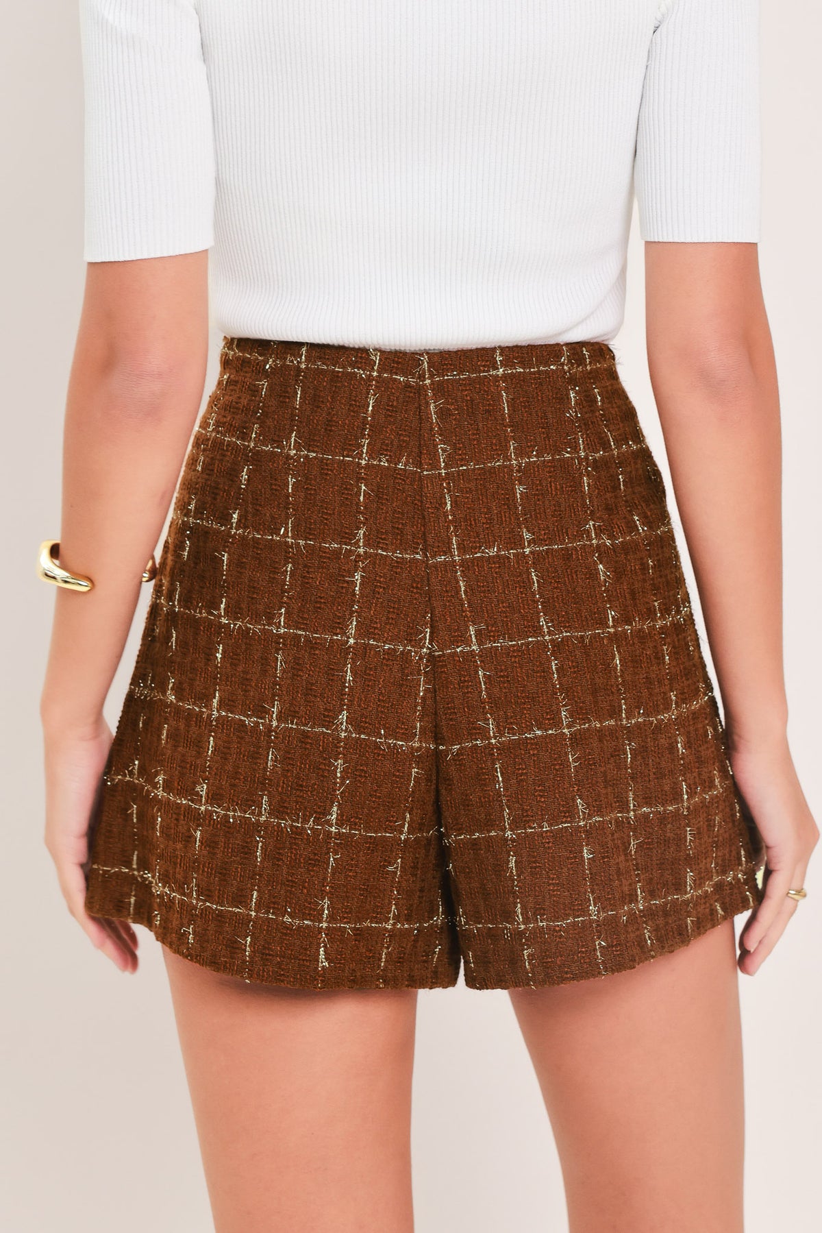 A model wearing a brown/rust tweed mini skort with a white windowpane plaid pattern and gold-tone buttons | Flying Tomato