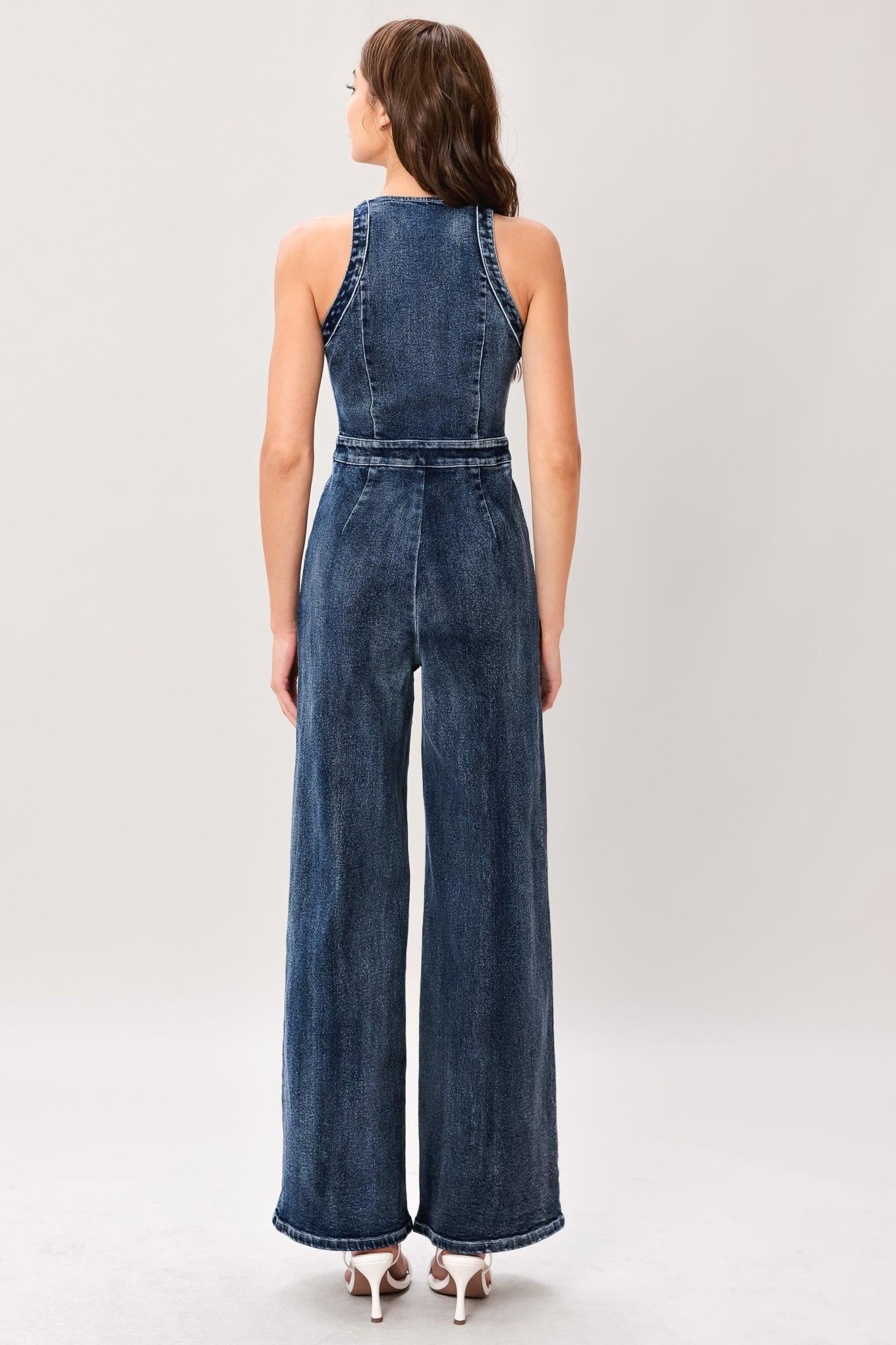 Woman wearing a washed denim jumpsuit featuring V neckline, front closure, center leg seam and straight leg