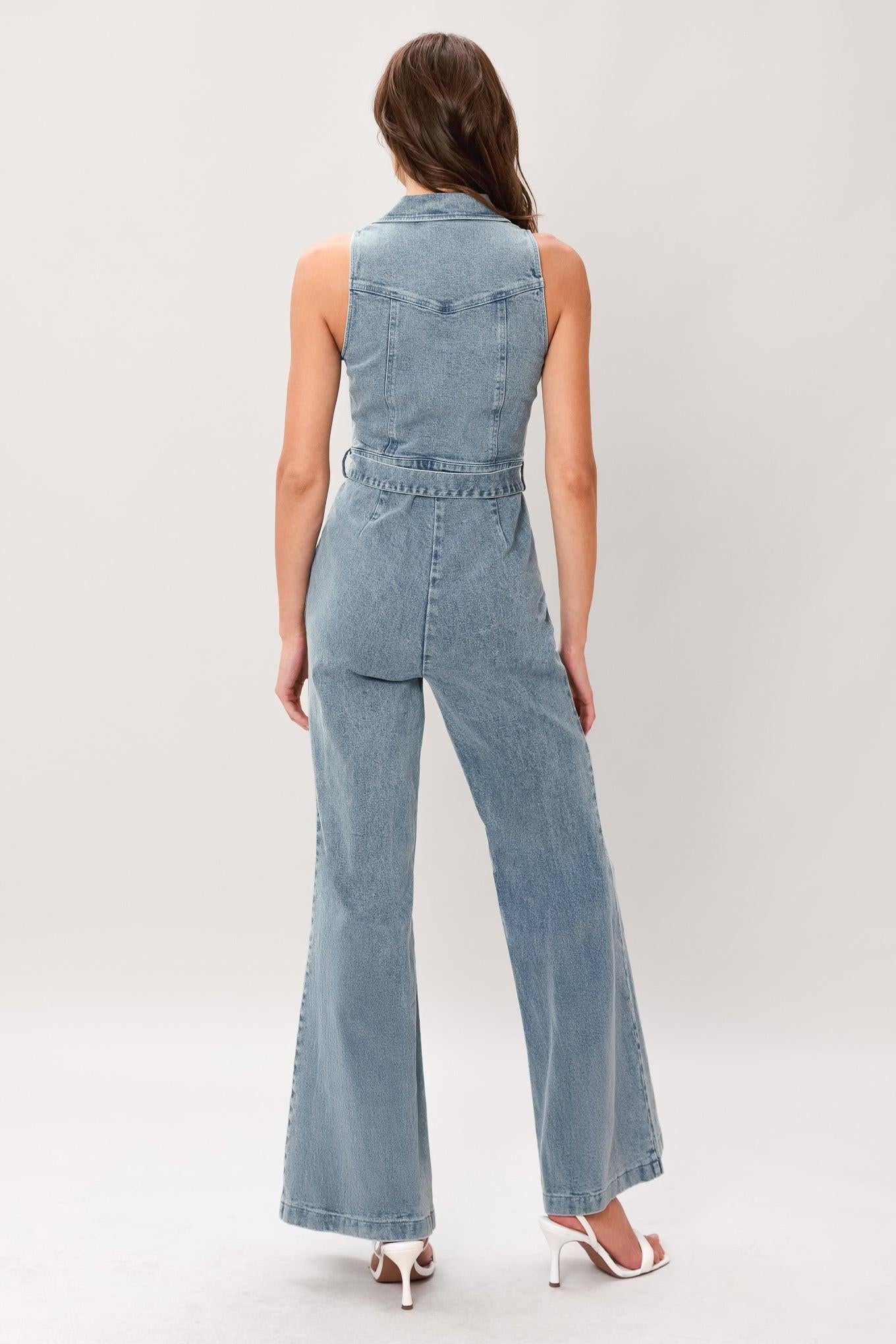 Woman wearing a washed denim jumpsuit featuring collar, sleeveless, front zipper, self belt and flare leg