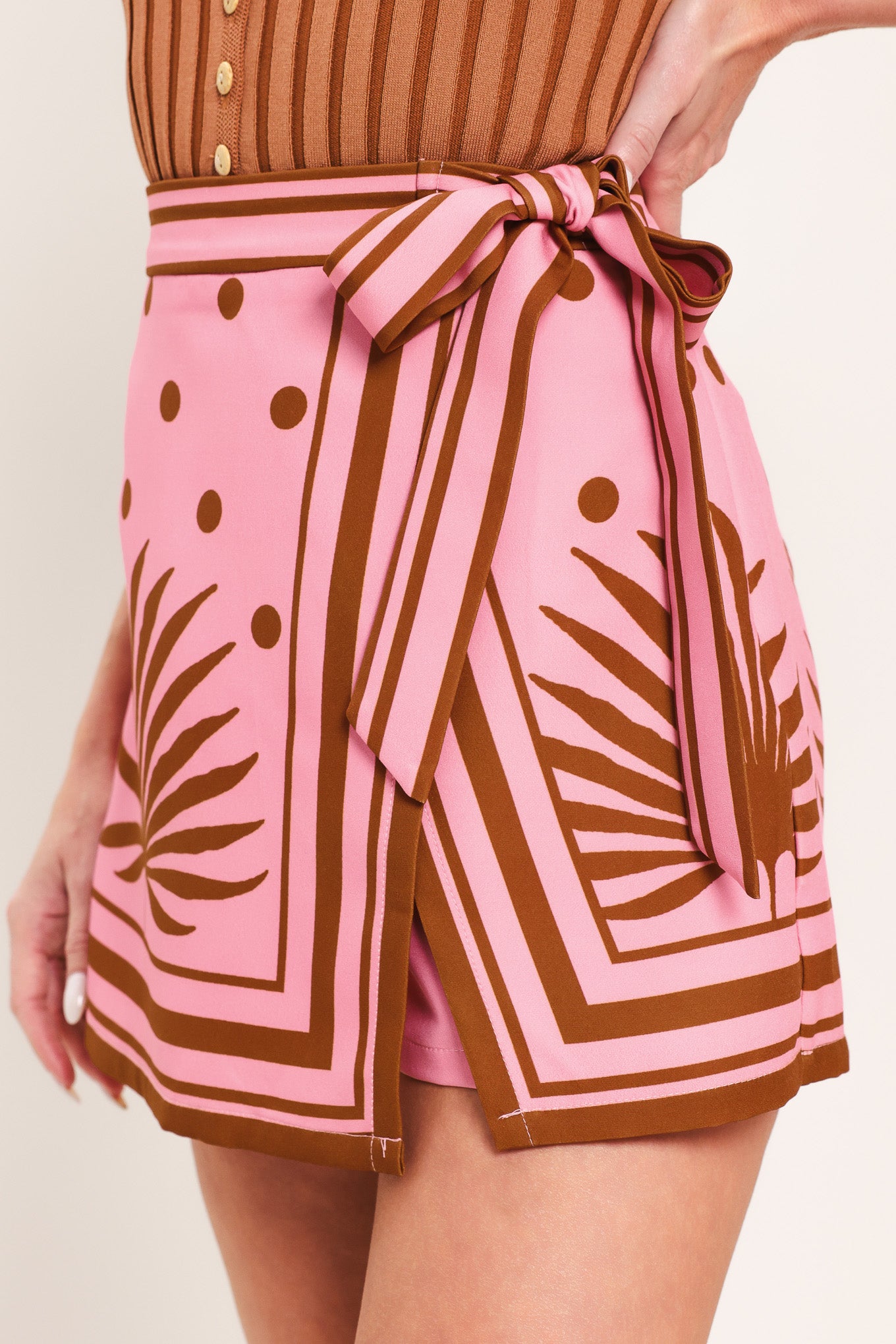 Woman wearing a pink skort with brown polka dots and printed palms featuring a side bow tie and zipper closure | Flying Tomato