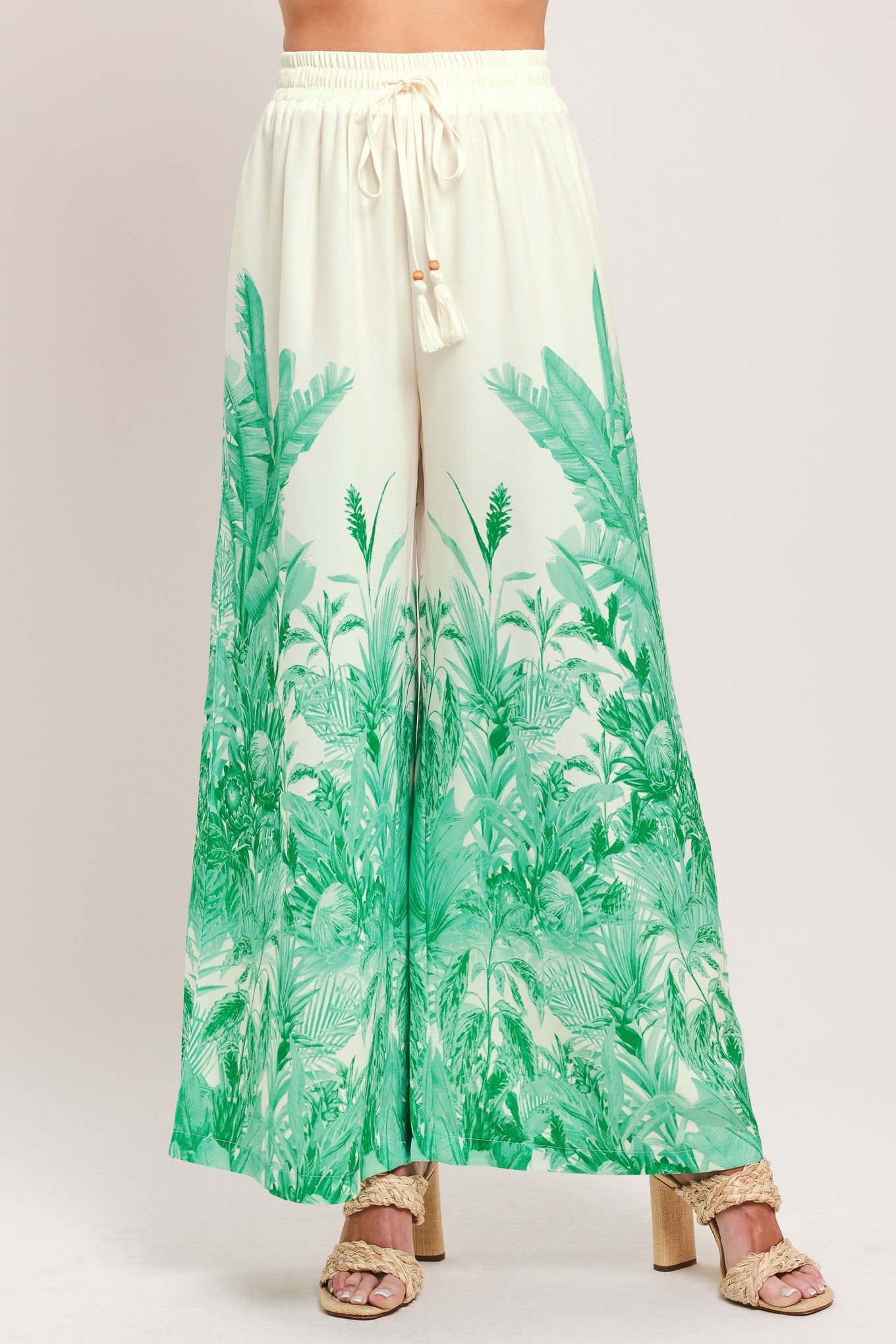 Woman wearing green and white tropical leaf patterned wide-leg pants with elastic waist and front tie | Flying Tomato