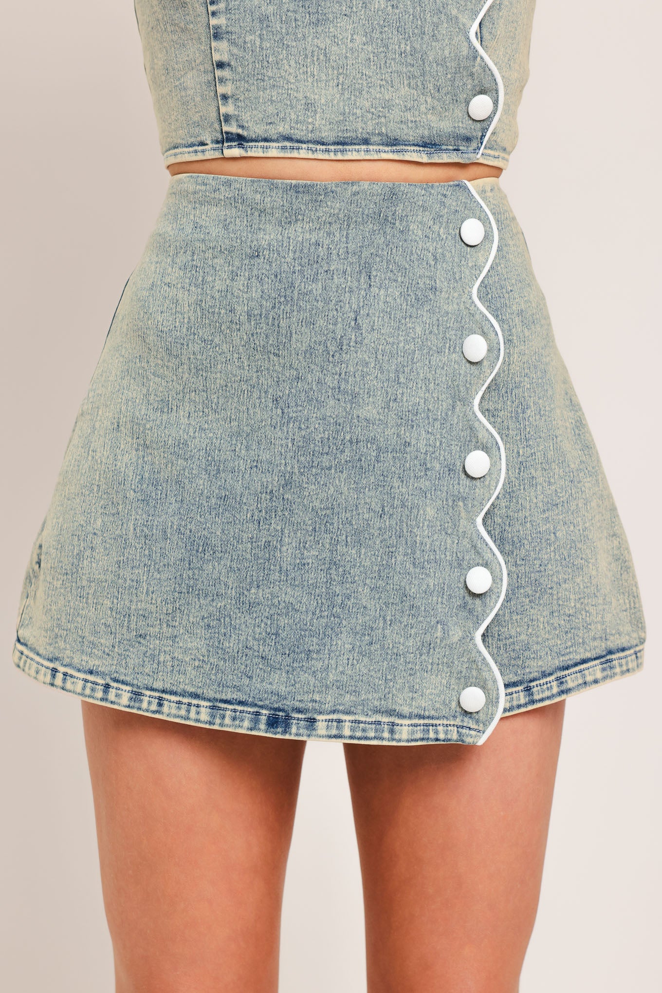 Woman wearing a denim skort featuring scallop edge with button and back zipper closure | Flying Tomato