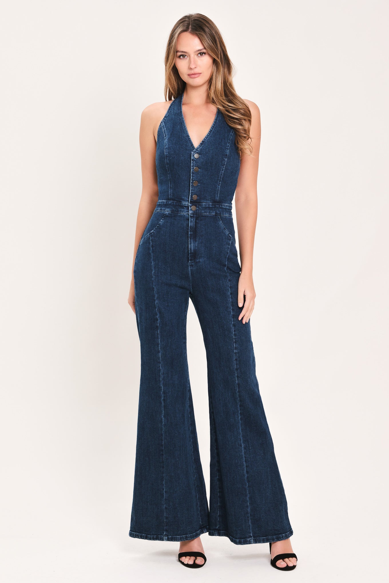 A woman wearing a dark blue denim halter jumpsuit with a button-front bodice and wide flared legs | Flying Tomato