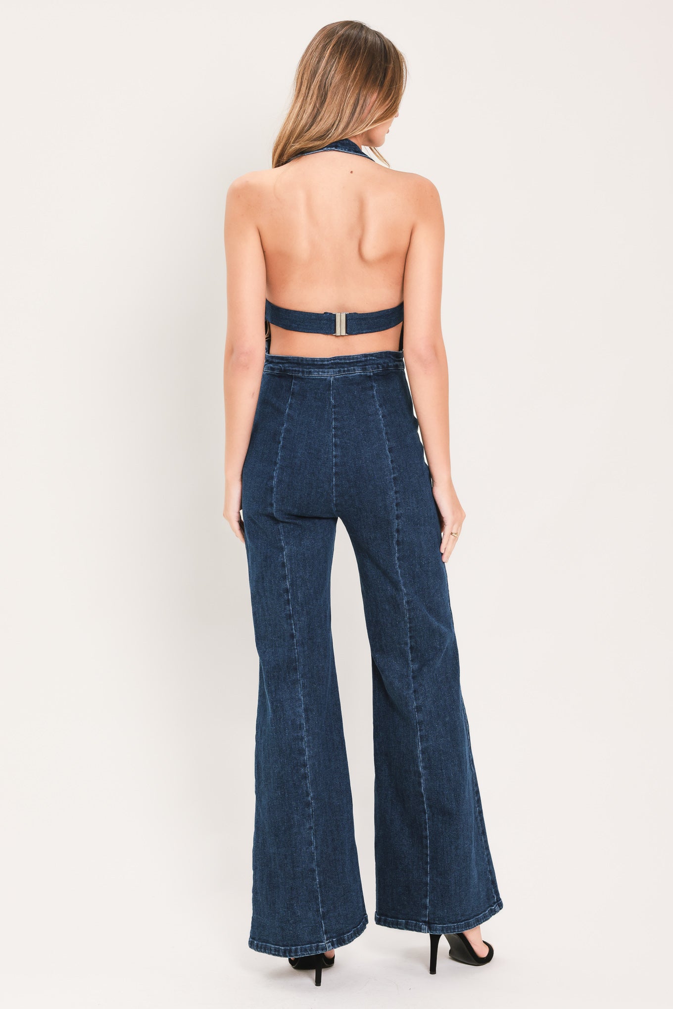 A woman wearing a dark blue denim halter jumpsuit with a button-front bodice and wide flared legs | Flying Tomato