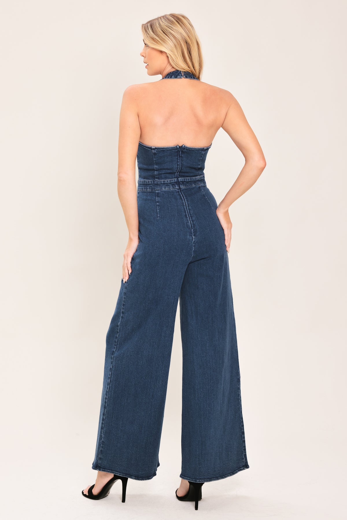 Woman wearing a denim jumpsuit featuring halter neckline, front button detail, wide leg, bare back and zipper closure | Flying Tomato