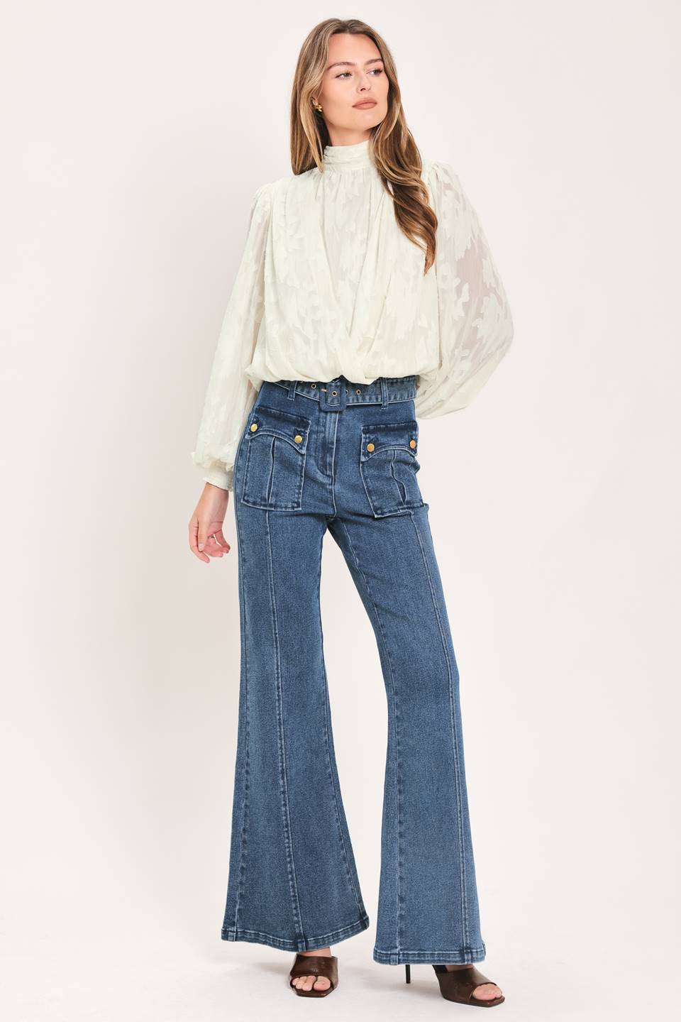 A woman wearing blue high-waisted flare jeans with front flap pockets and gold-tone button details | Flying Tomato