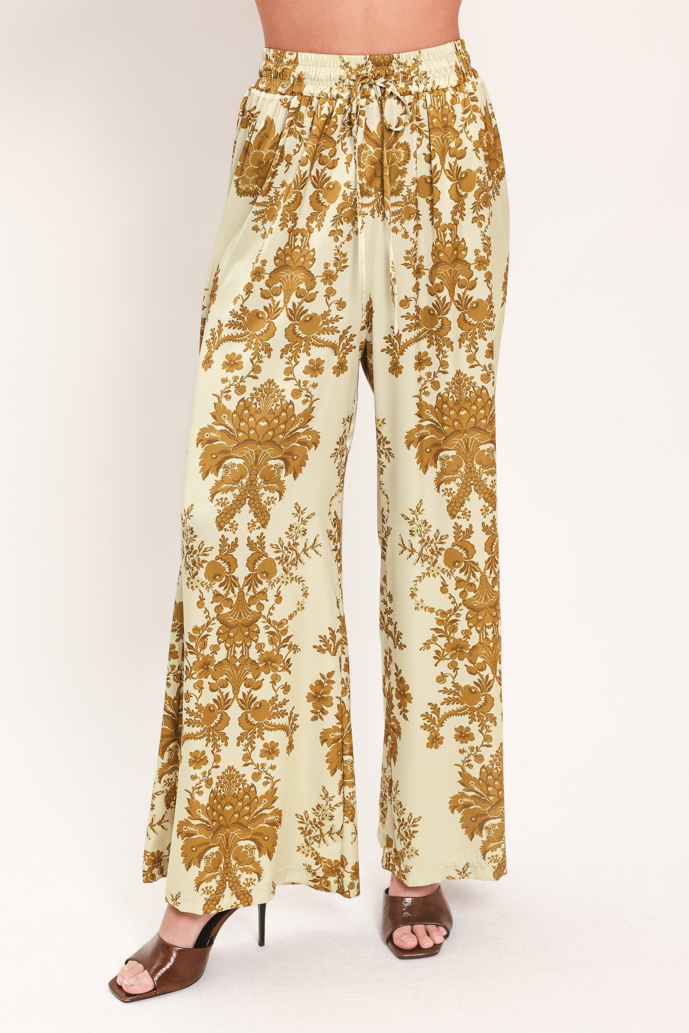 A woman wearing high-waisted, wide-leg pants with a beige base and an ornate gold damask pattern | Flying Tomato