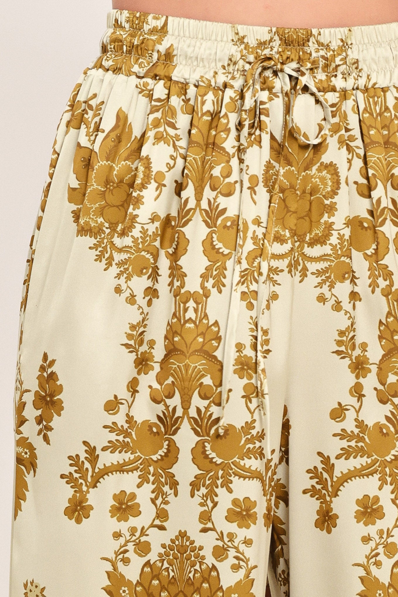 A woman wearing high-waisted, wide-leg pants with a beige base and an ornate gold damask pattern | Flying Tomato