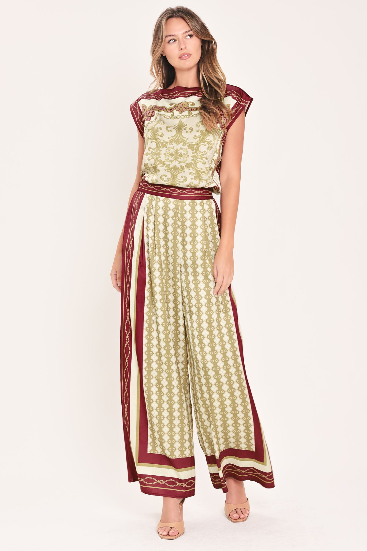 A woman wearing a pair of wide-leg pants with a beige and gold geometric pattern, featuring deep burgundy side panels and a matching patterned hem | Flying Tomato