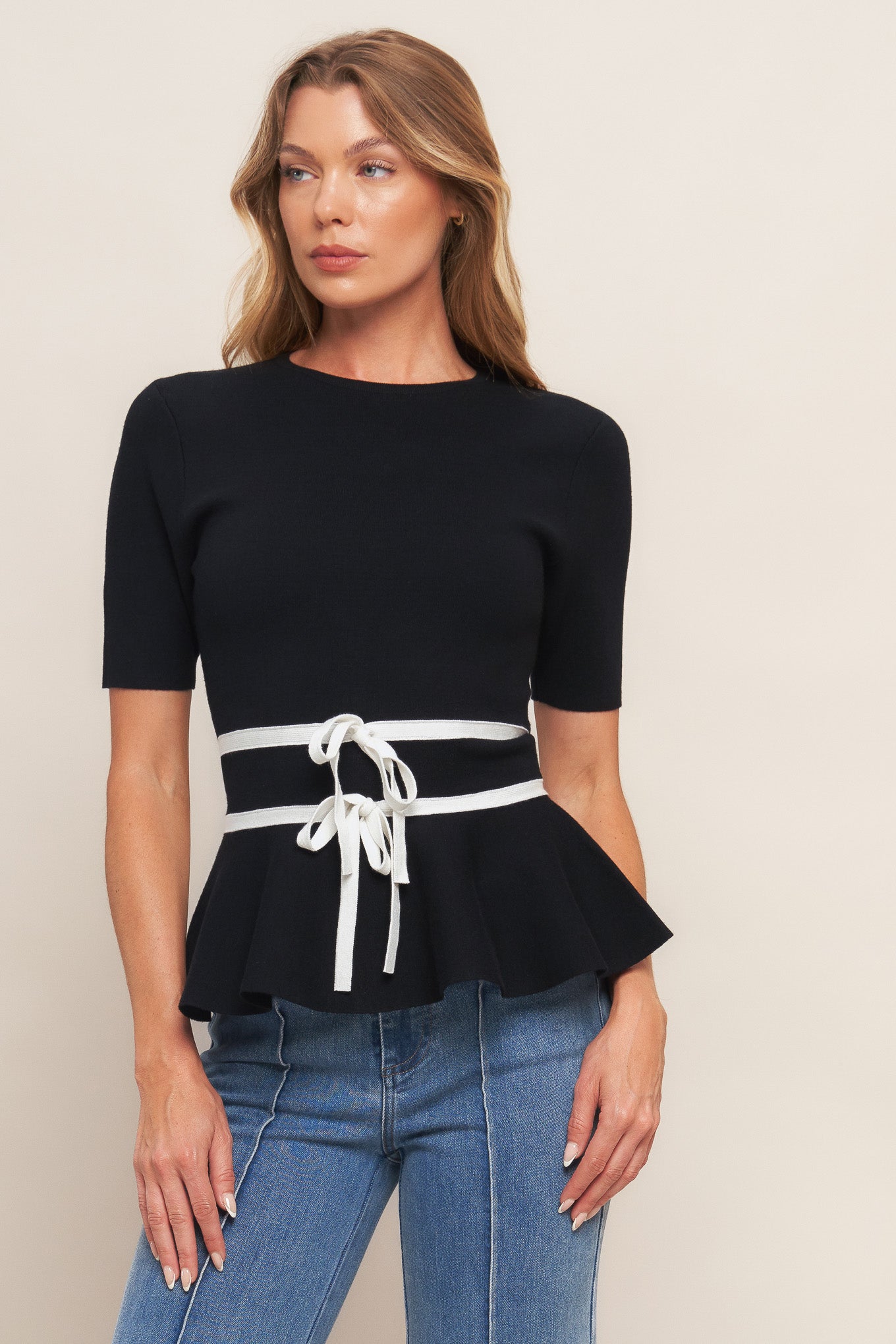 A solid sweater knit top featuring round neckline, short sleeve, bow front, peplum and back zipper closure