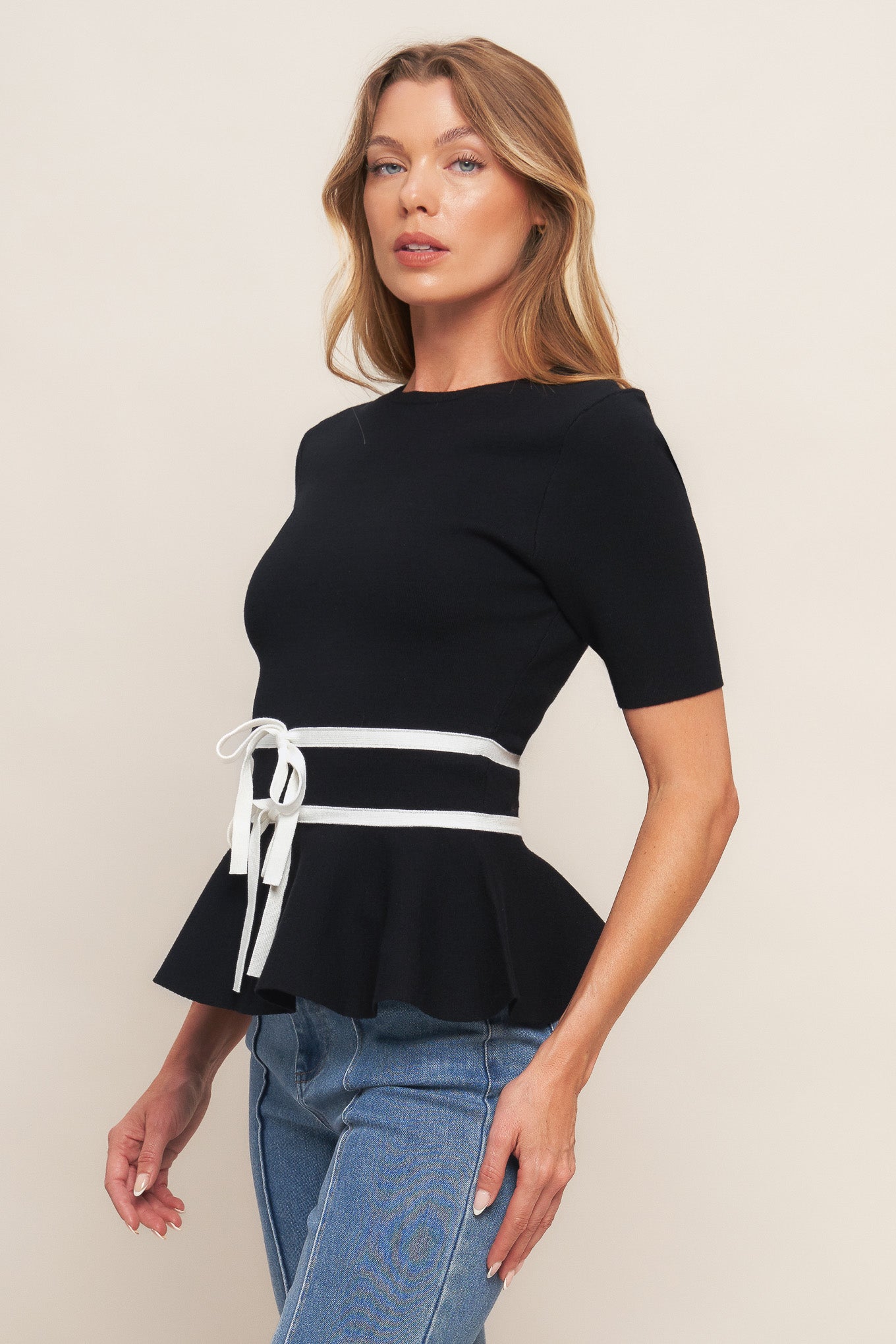 A solid sweater knit top featuring round neckline, short sleeve, bow front, peplum and back zipper closure